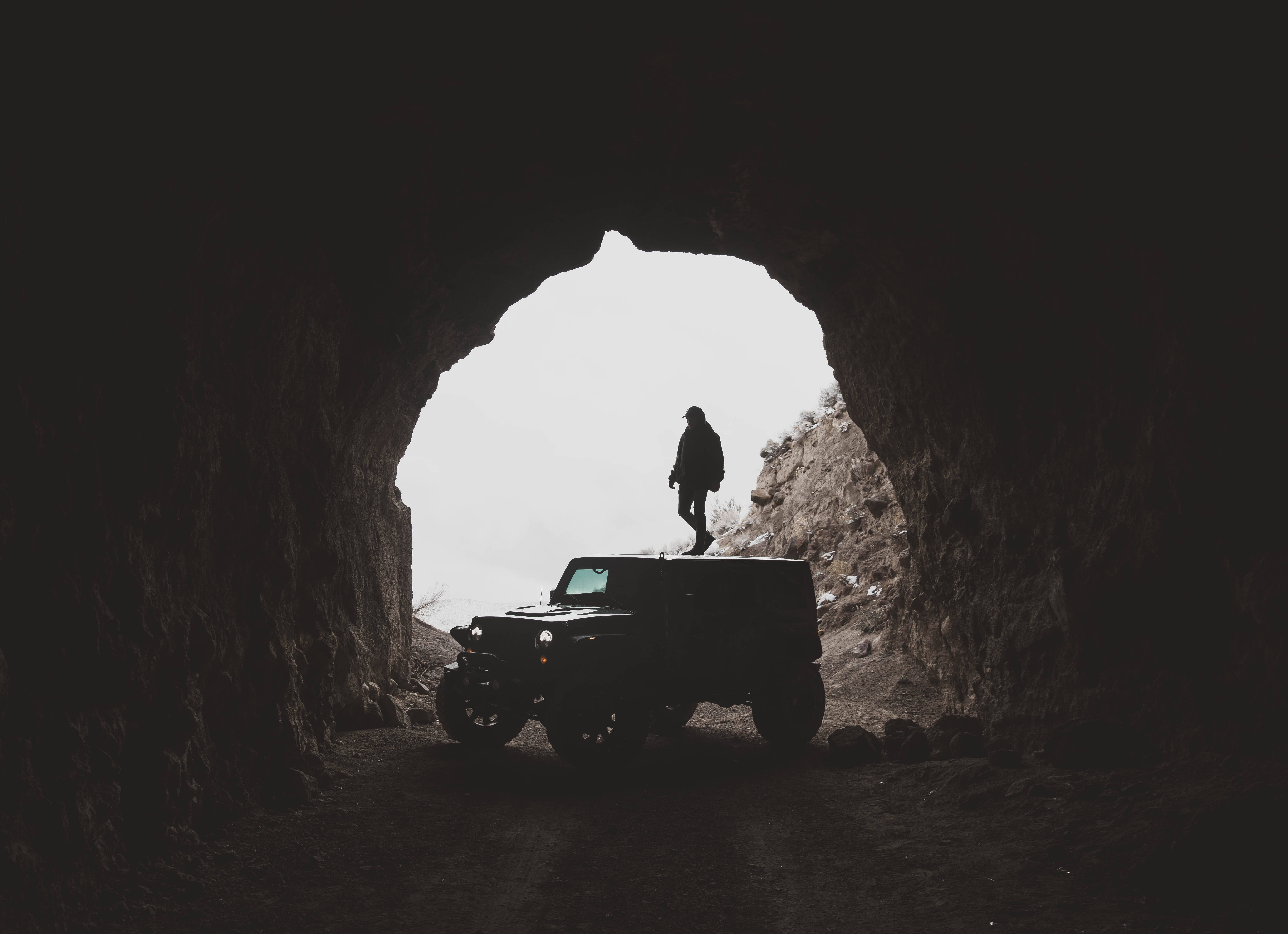 SUV Jeep 壁紙 — 一個人和一輛堅固的吉普車的剪影，以岩石洞穴入口為框，背後是明亮的日光。