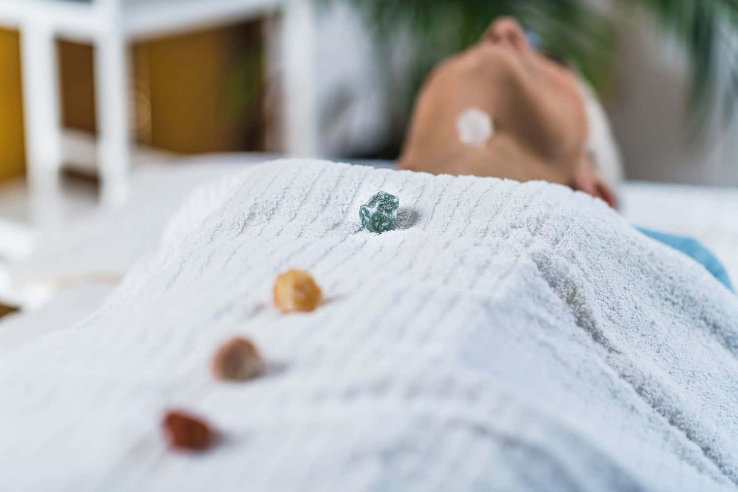 Reiki 桌布 壁紙 — 一個人喺有紋理嘅白色毯下面平靜咁休息，彩色石頭排成一排。