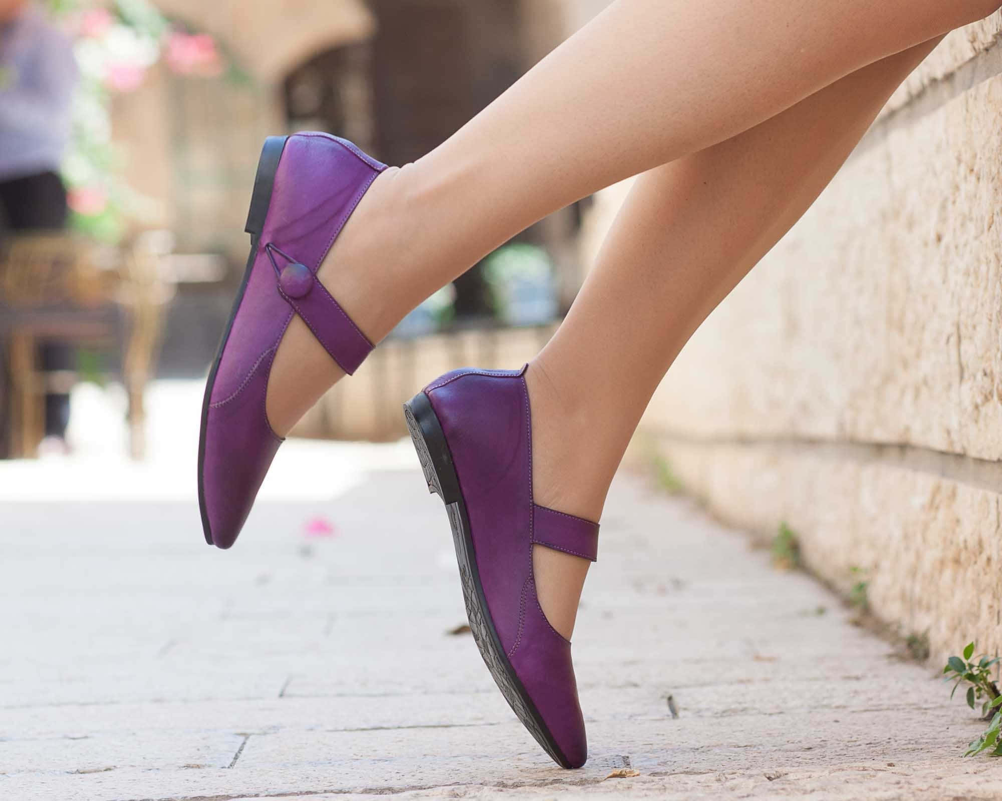 Purple Shoes 桌布 壁紙 — 一個人嘅腳近鏡，著住鮮艷紫色嘅腳踝鞋，喺陽光普照嘅鵝卵石小徑上，隨意咁靠喺石牆邊。