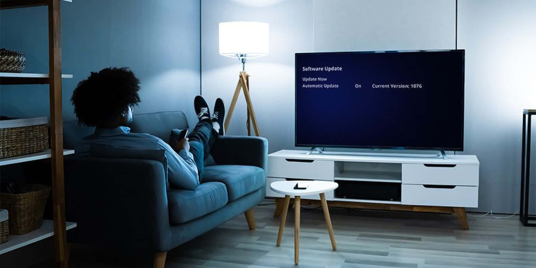 Home Entertainment 桌布 壁紙 — 一個人在光線昏暗的現代客廳的藍色沙發上休息，觀看顯示軟體更新畫面的電視。