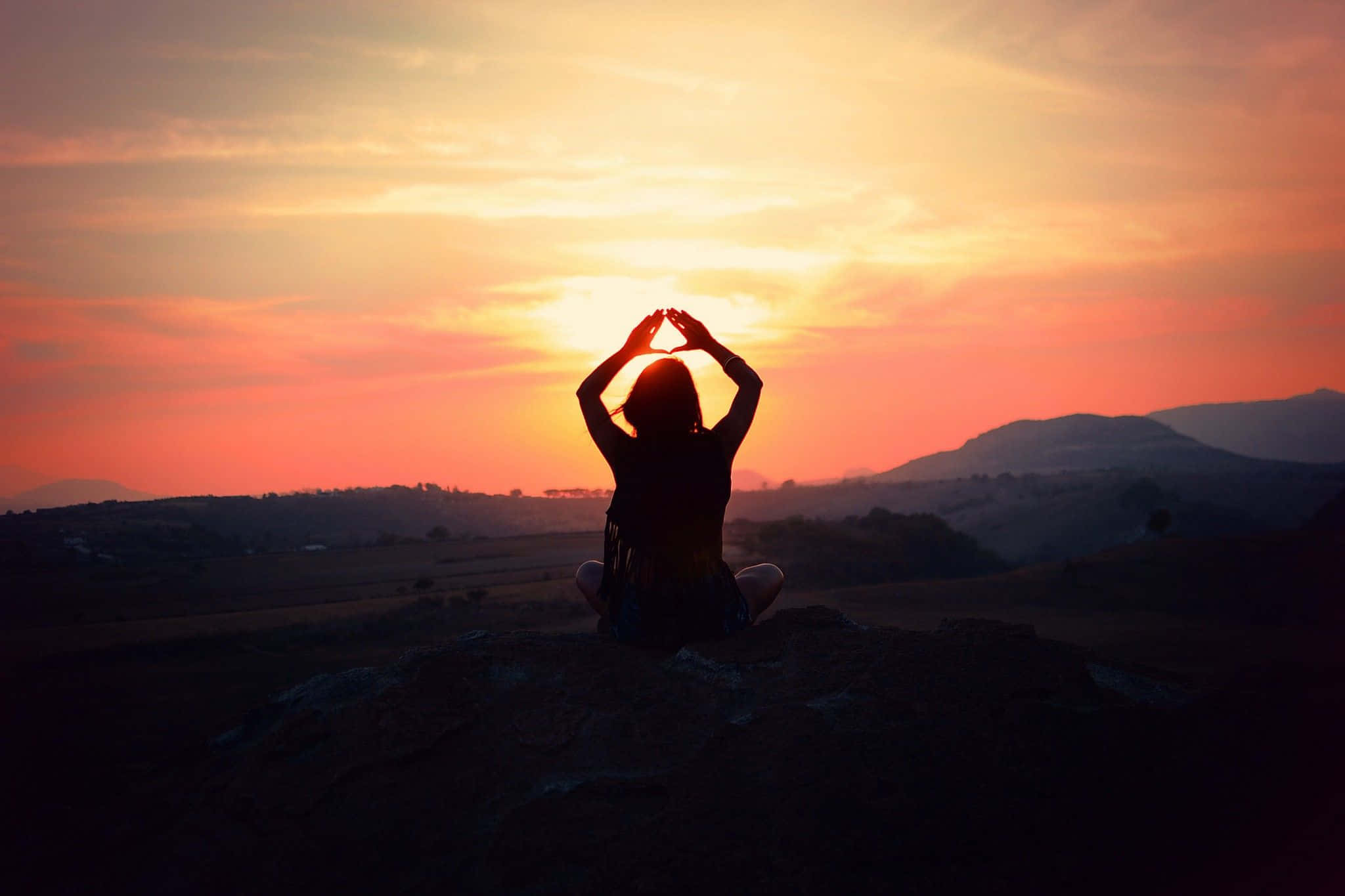 Transcendental 桌布 壁紙 — 一個人在山頂上冥想，夕陽以火熱的橙色和粉紅色調落下，形成剪影。