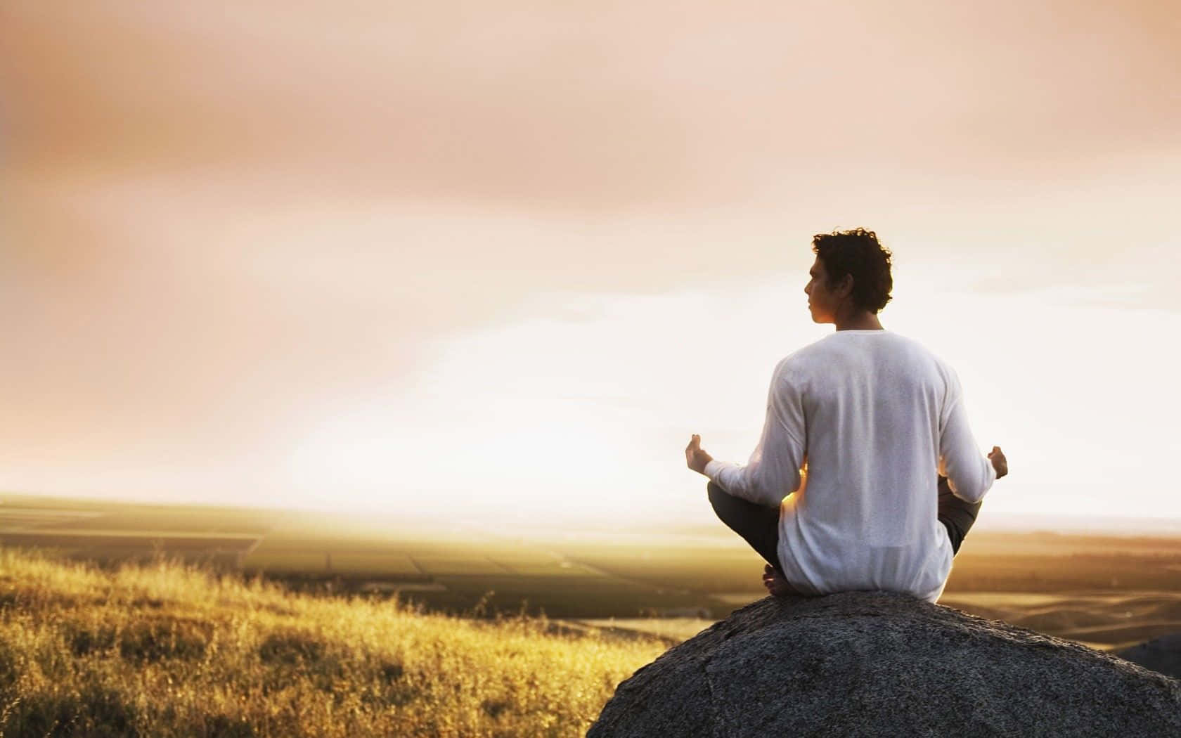 Transcendental 桌布 壁紙 — 一個人在日落時分以蓮花坐姿坐在岩石上，俯瞰金色田野。