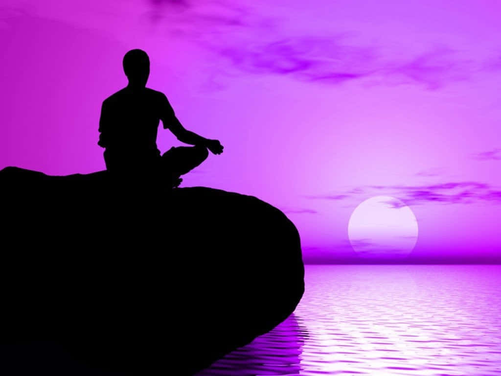 Spiritual Meditation 桌布 壁紙 — 一個人在日落時分在岩石上冥想，背景是充滿活力的紫色天空和水面倒影的剪影。
