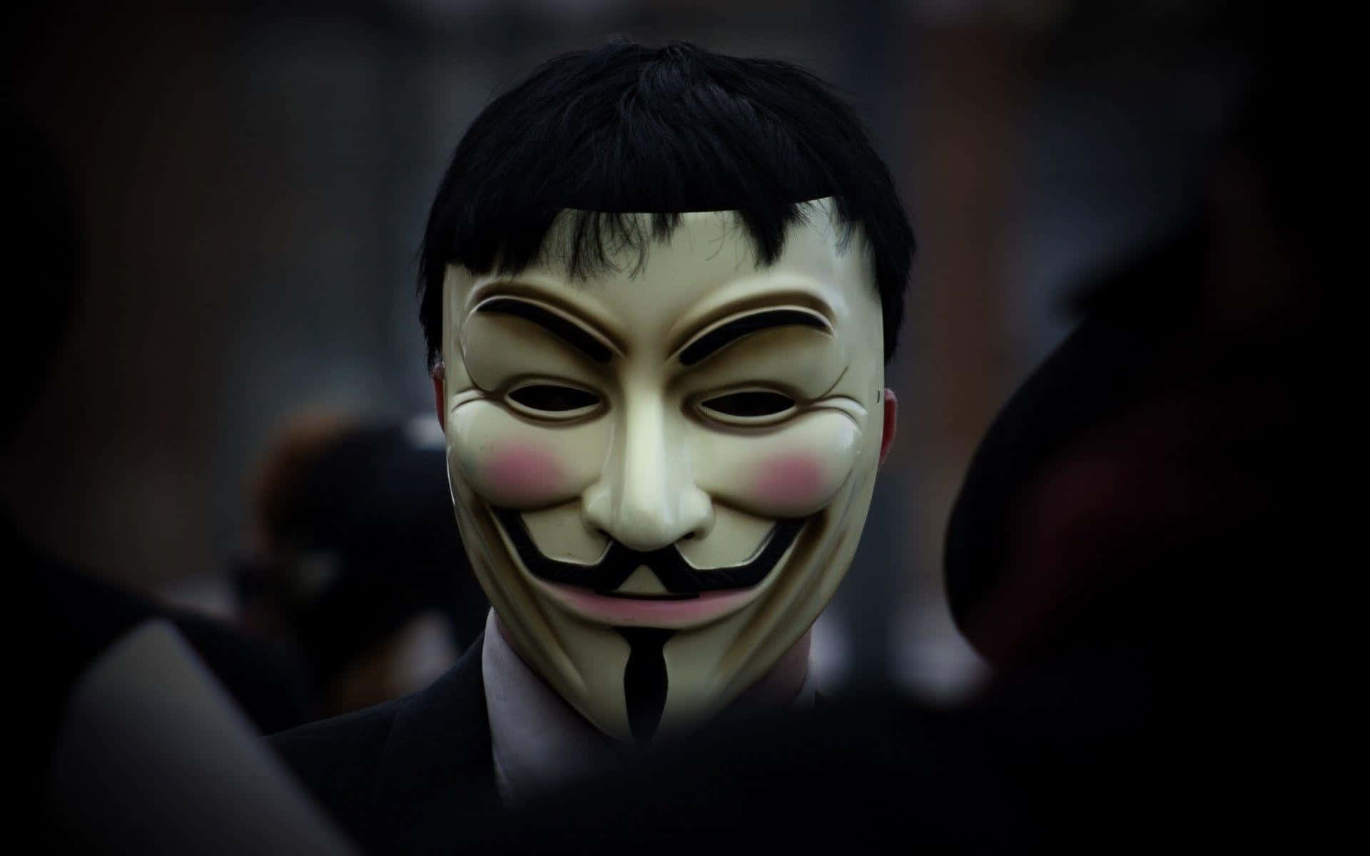 Anonymous 桌布 壁紙 — 一個人在昏暗的人群中戴著白色 Guy Fawkes 面具，臉頰粉紅，鬍子黑色。