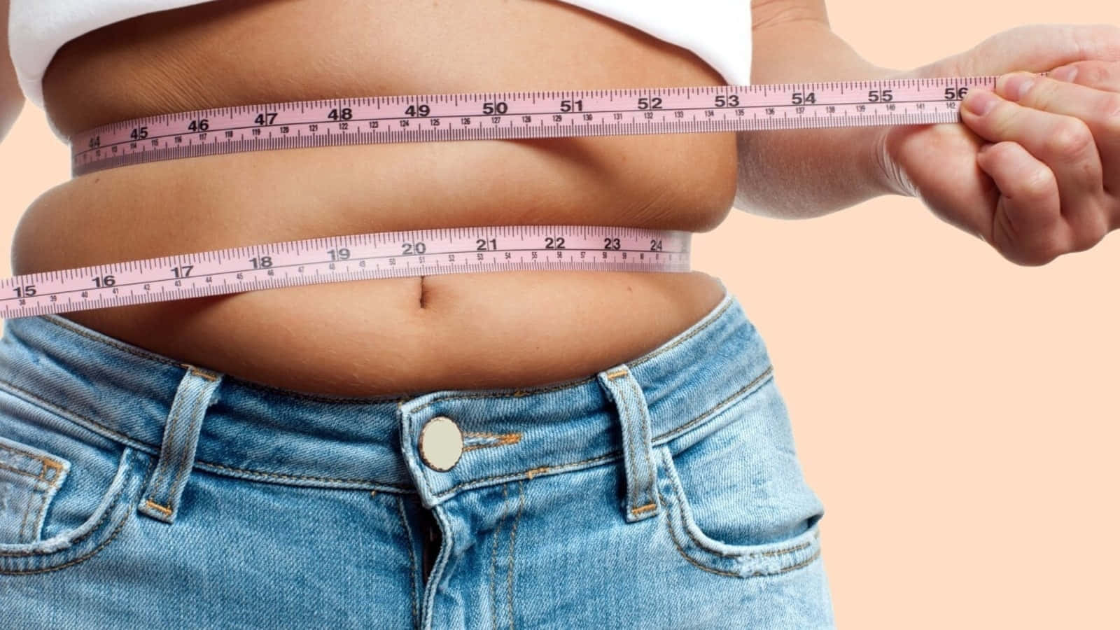 Weight Loss 桌布 壁紙 — 一個人在柔和蜜桃色背景上用粉紅色軟尺量度腰圍。
