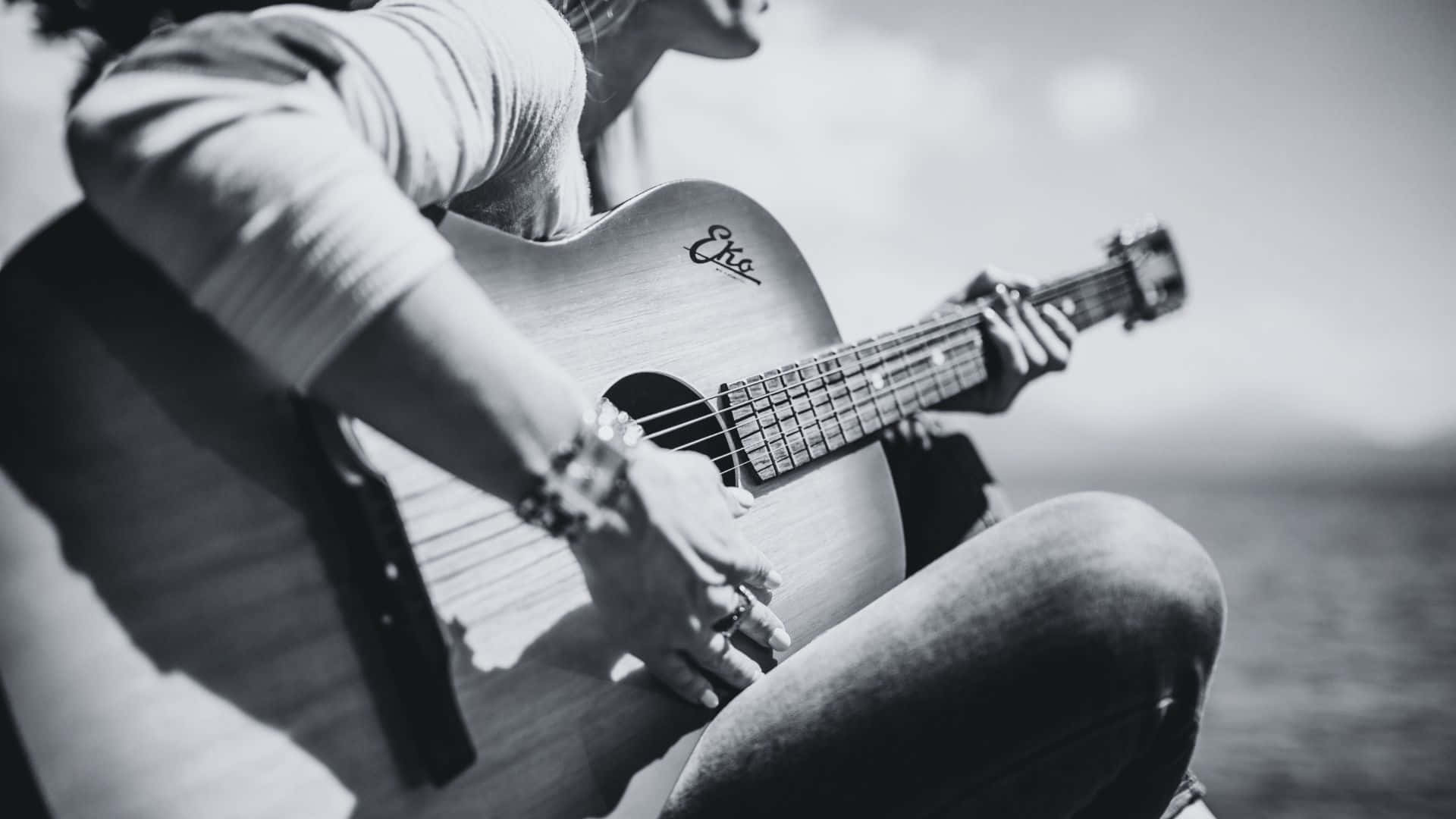 Black And White Guitar 桌布 壁紙 — 一個人在水邊彈奏黑白原聲結他，柔和陽光灑落。