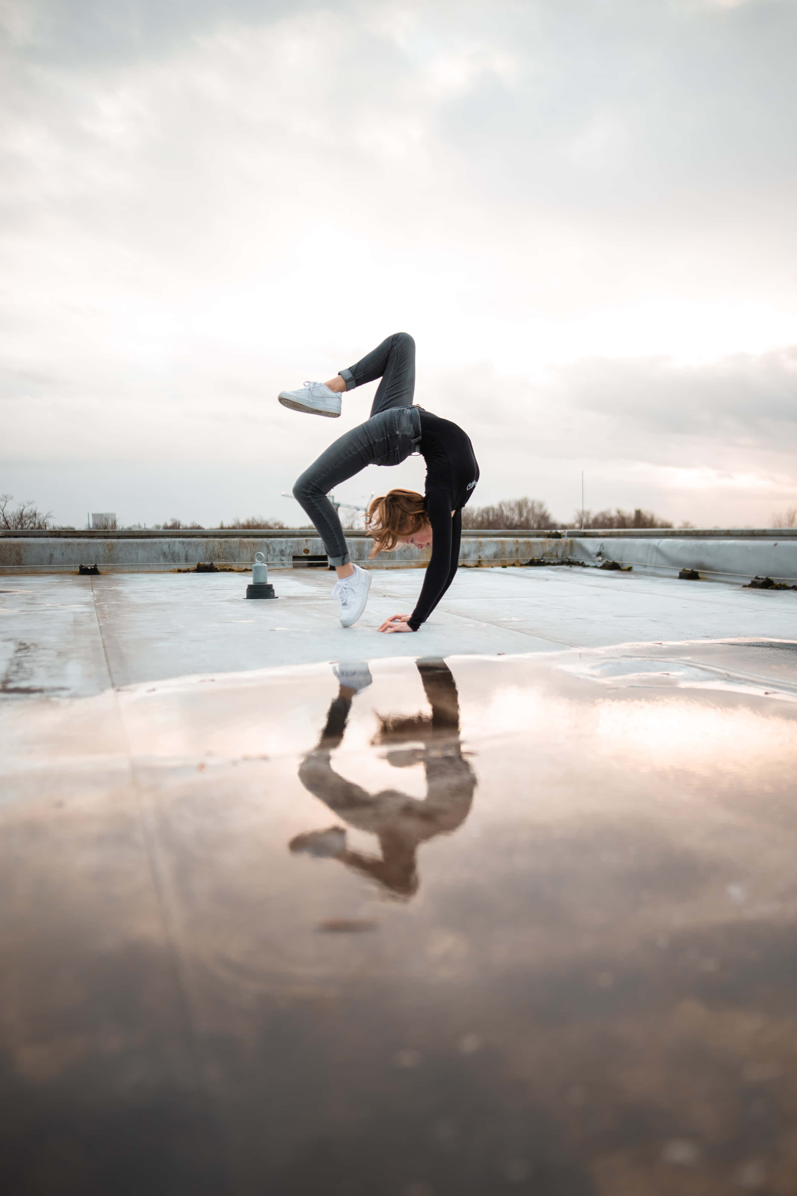 Gymnastics 桌布 壁紙 — 一個人在潮濕的屋頂上做出充滿動感的倒立動作，水坑中清晰倒映出身影，天空多雲。