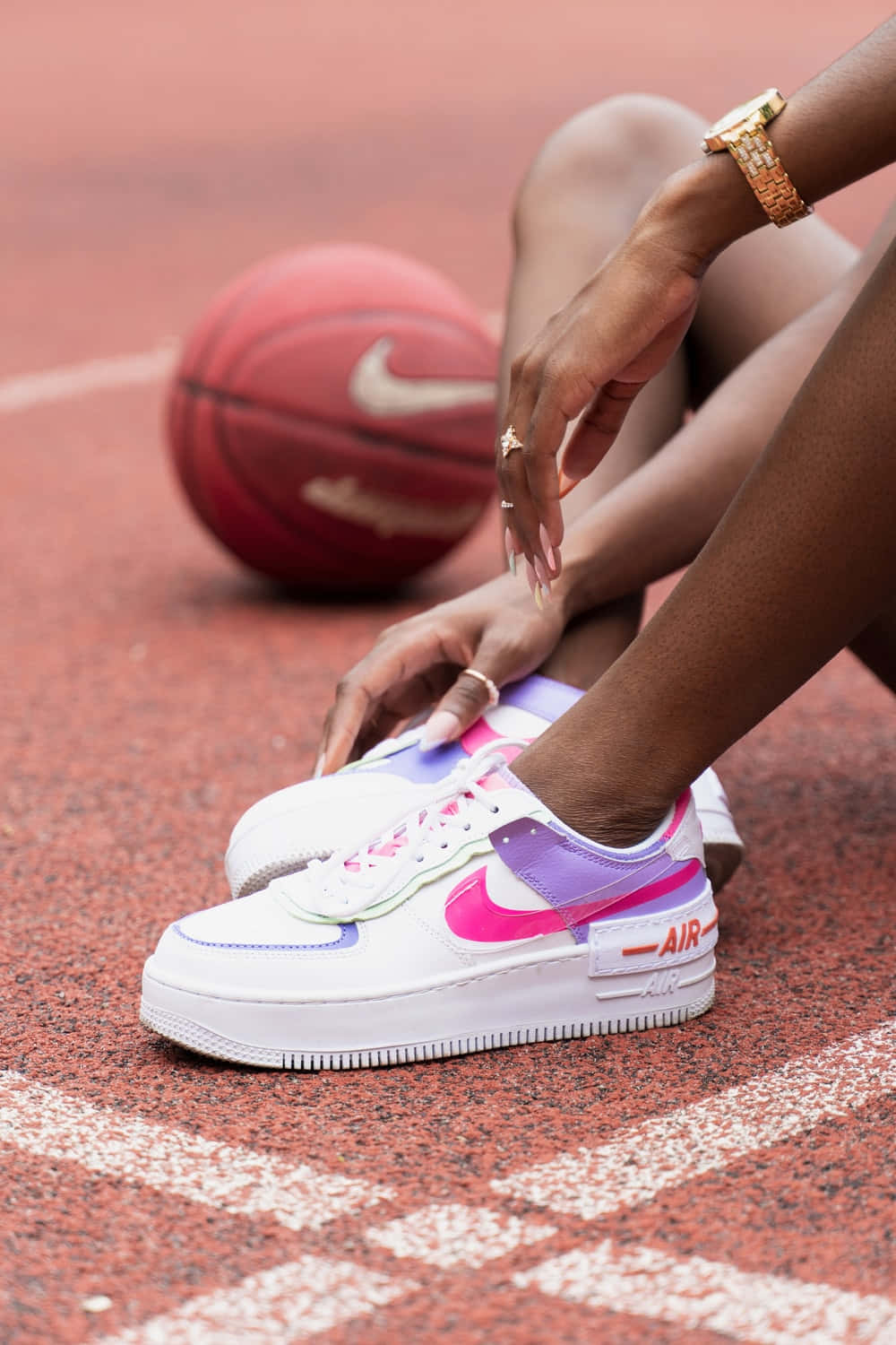 Cute Shoes 桌布 壁紙 — 一個人在紅色籃球場上調整鮮豔的粉紅色和紫色運動鞋，附近有一個球。