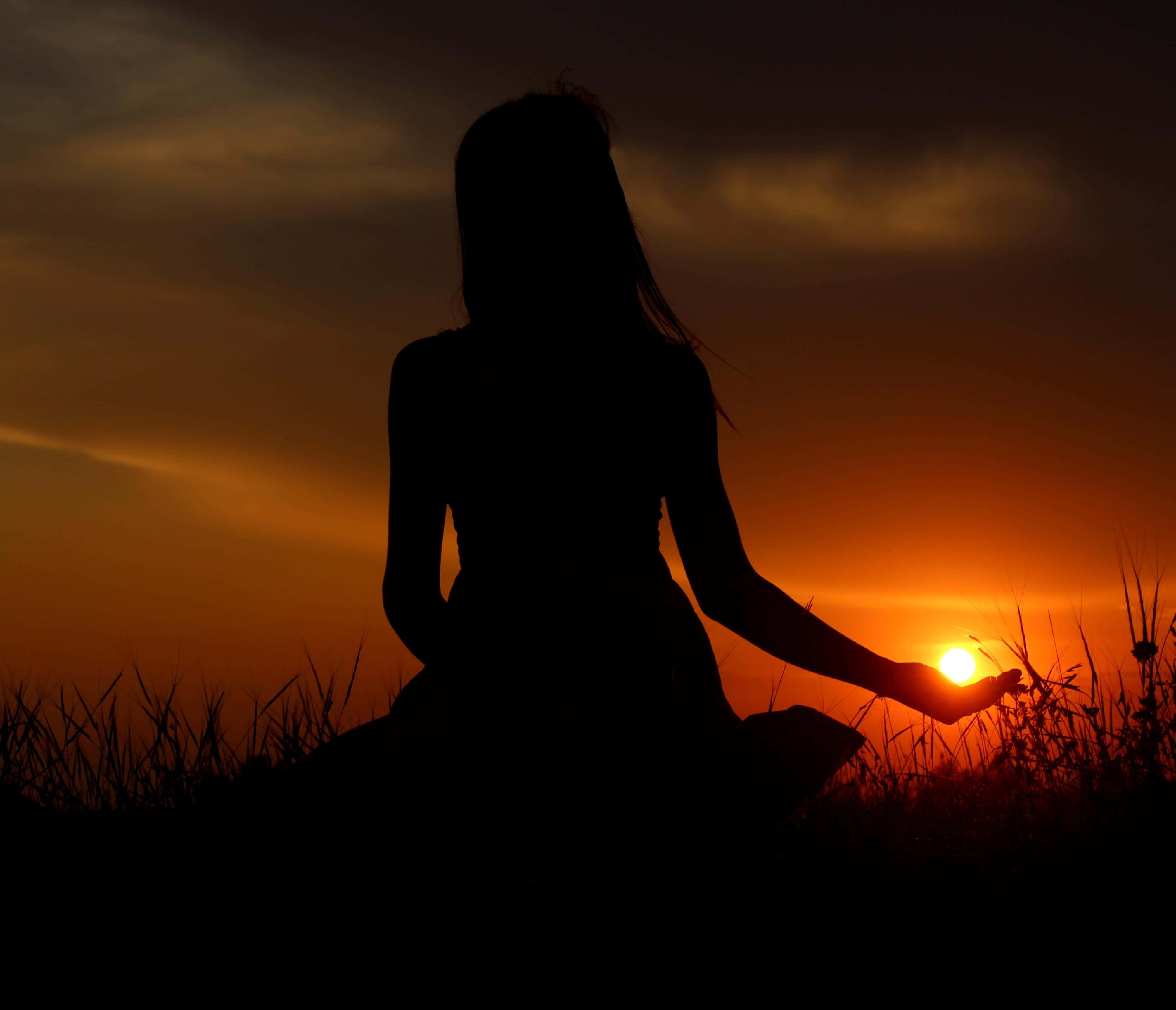 Sunset Silhouette 桌布 壁紙 — 一個人在草地上冥想，夕陽在他們伸出的手後方落下，形成剪影。