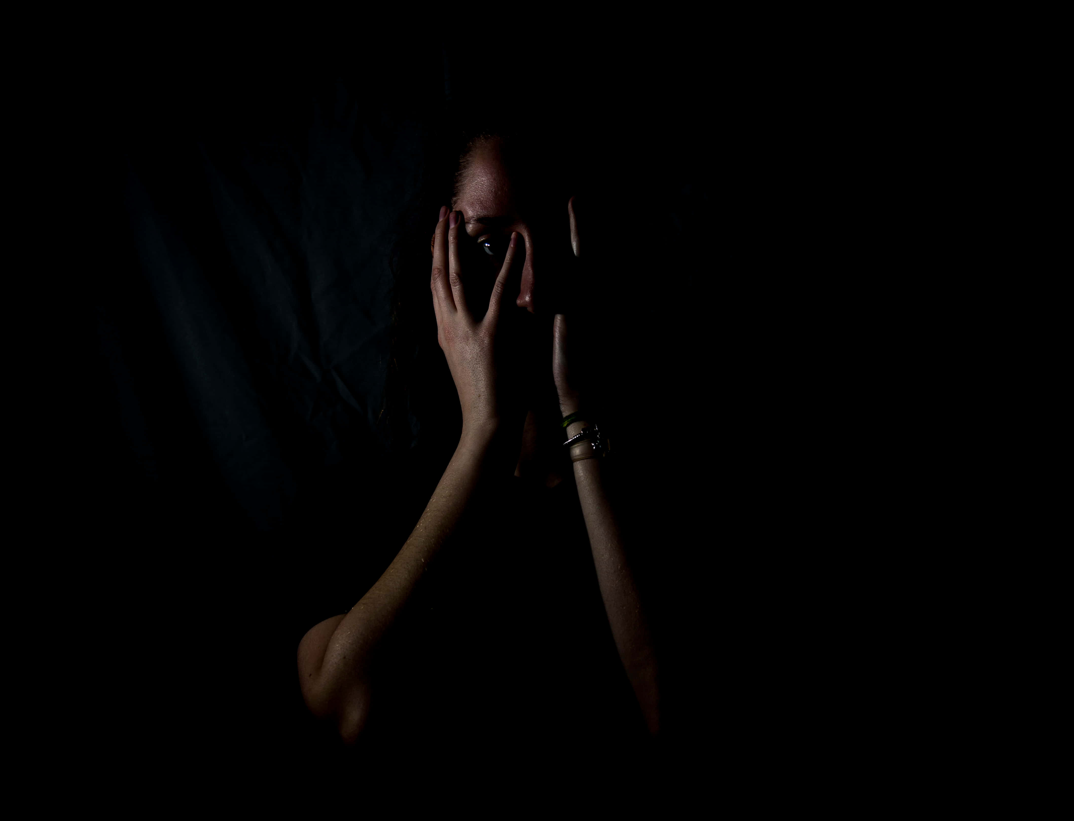 Dark Fear 桌布 壁紙 — 一個人在近乎全黑的環境中用手遮住臉，只露出一隻眼睛，戲劇性的低調燈光。
