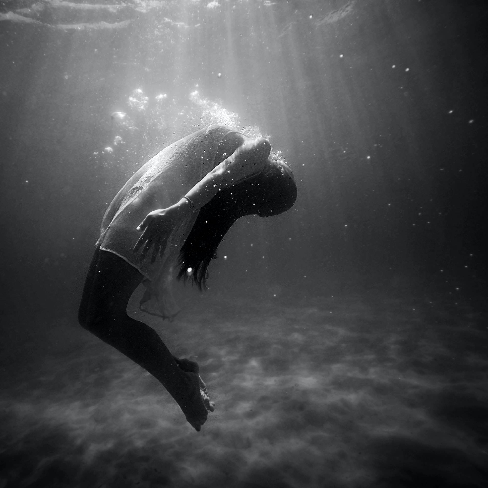 photography 桌布 壁紙 — 一個人在黑白畫面中潛入水底，陽光穿透水面，身後留下氣泡。