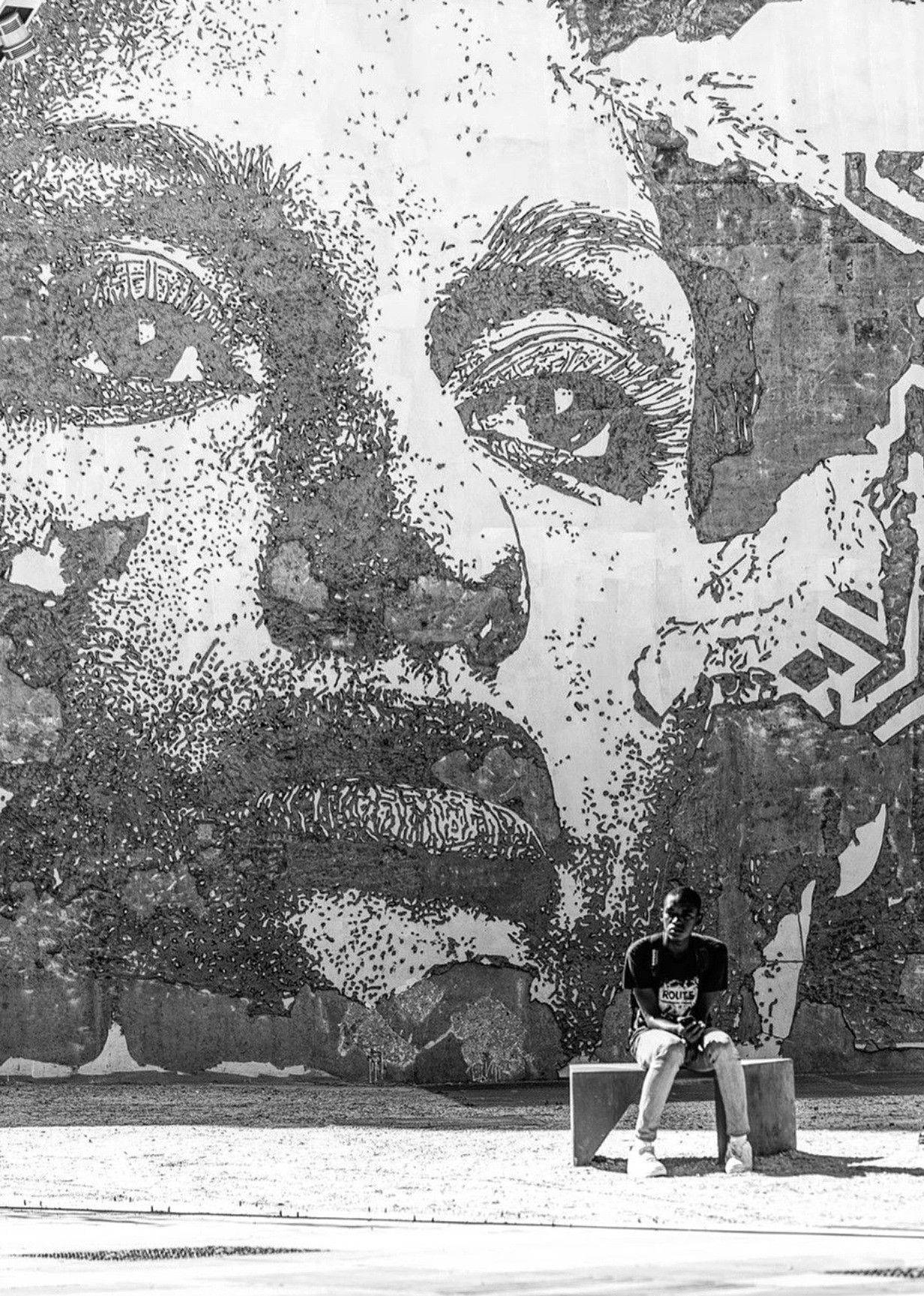 Black And White Graffiti 桌布 壁紙 — 一個人坐在長椅上，面前是城市牆上一個巨大黑白點陣式人臉壁畫。
