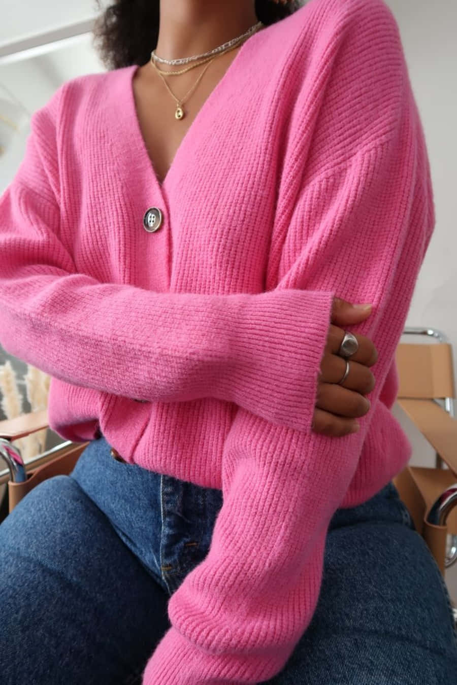 Pink Sweater 桌布 壁紙 — 一個人坐著，身穿鮮豔的粉紅色羅紋針織開衫，單顆鈕扣，搭配多層項鍊。