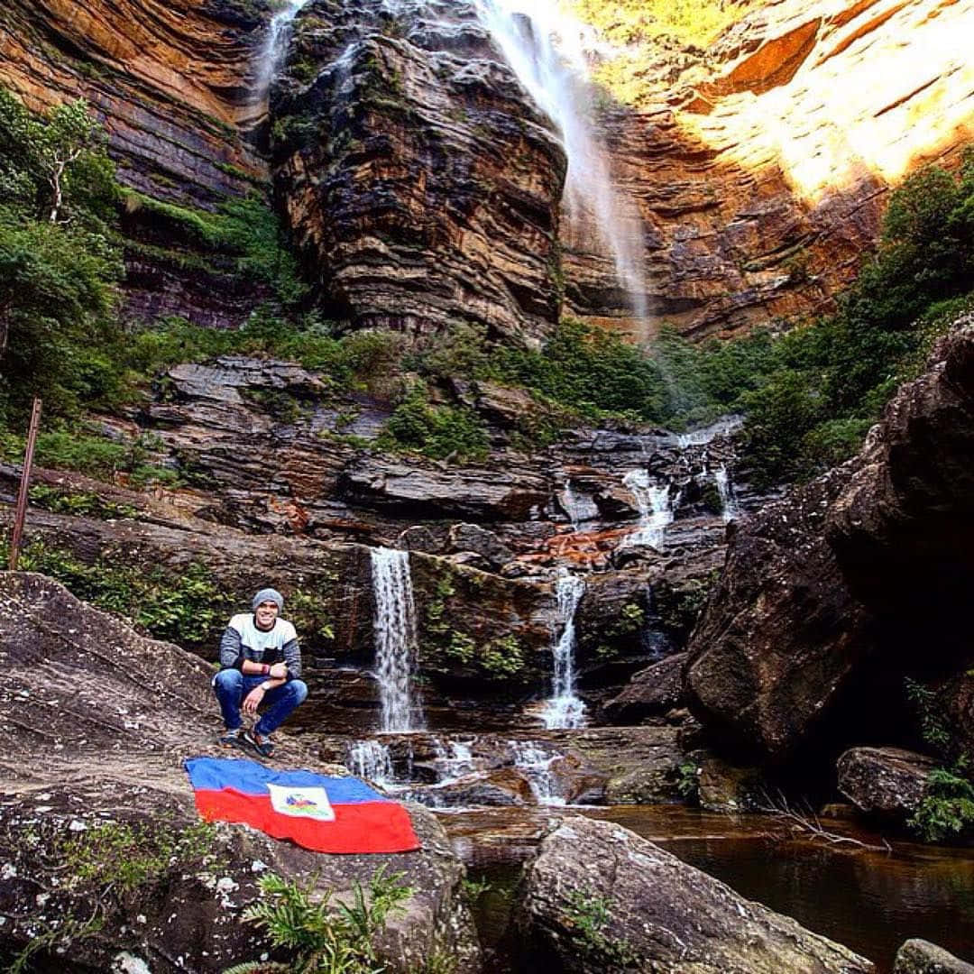 Blue Mountains National Park 桌布 壁紙 — 一個人平靜地坐在崎嶇峽谷中的瀑布前，周圍有茂密的綠色植物和層狀岩層。