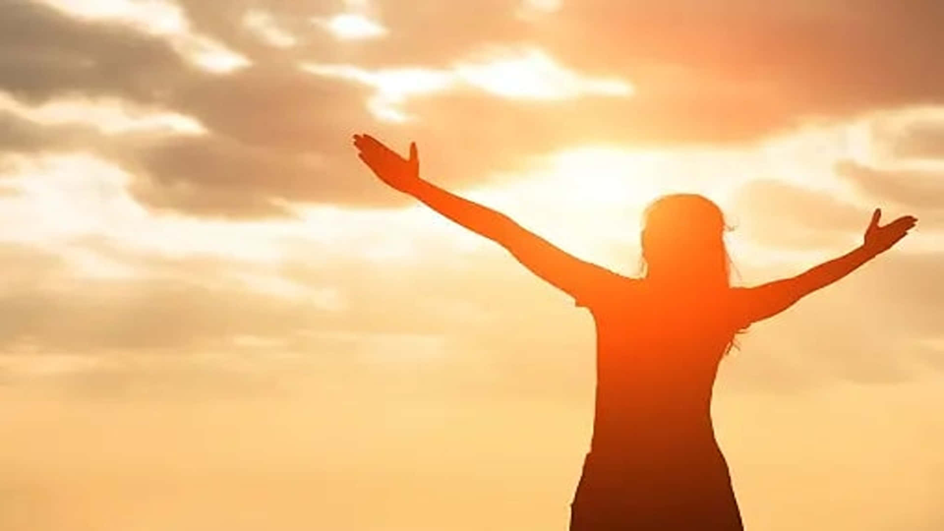 Eternal Life 桌布 壁紙 — 一個人張開雙臂，站在燦爛的日落天空前，在溫暖的金色光芒中形成剪影。