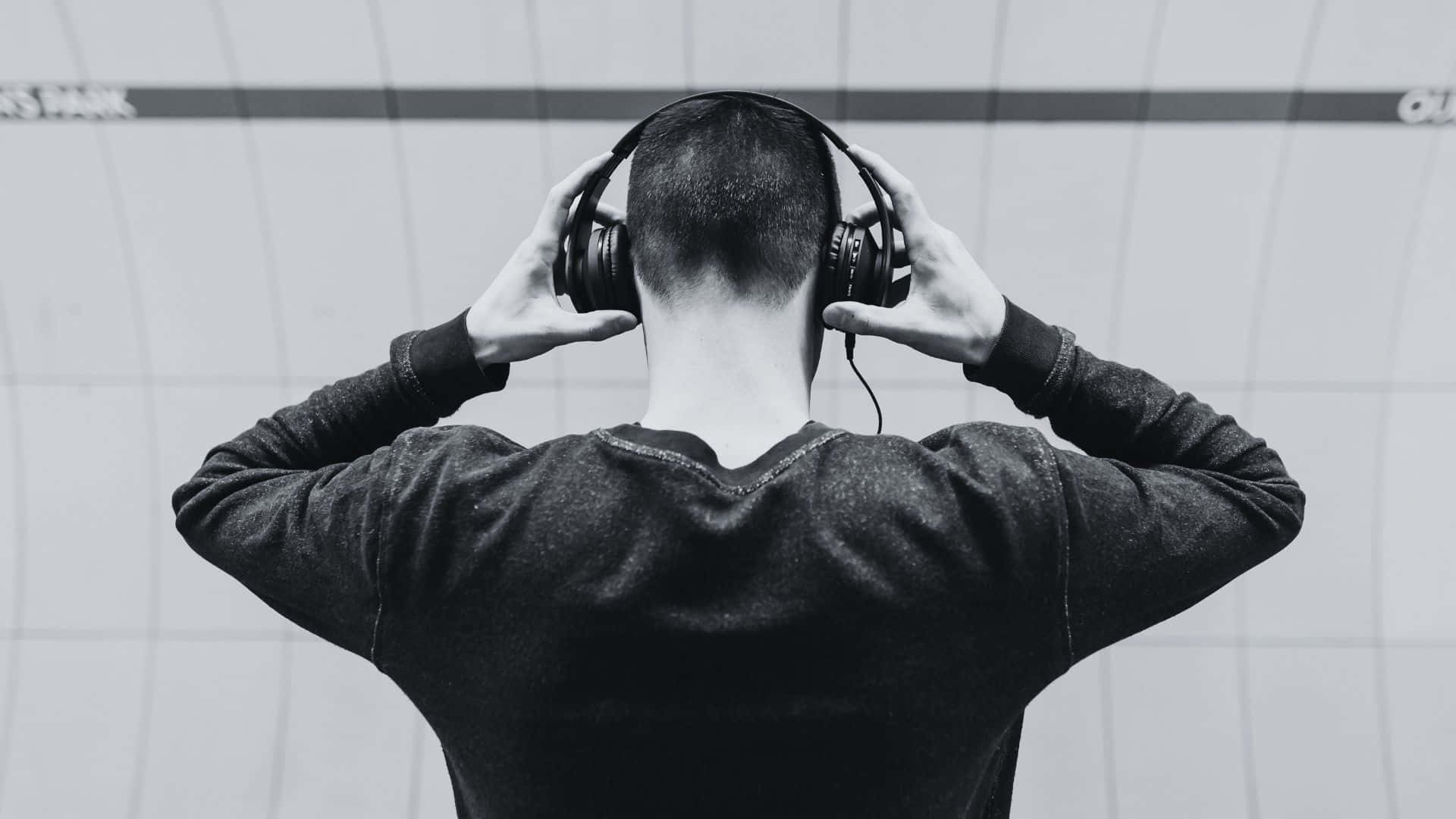Black And White Music 桌布 壁紙 — 一個人從背後調整頭戴式耳機，背景係瓷磚牆，黑白風格。