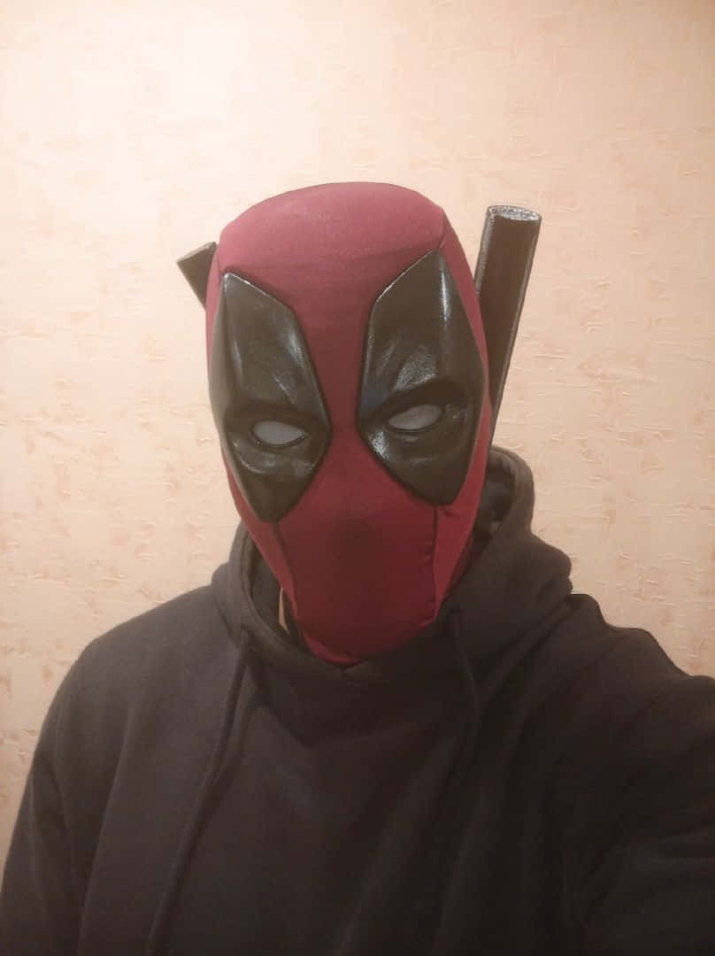 Deadpool Mask 桌布 壁紙 — 一個人戴住紅黑色死侍面具，背上綁住兩把武士刀，企喺米白色牆前面。