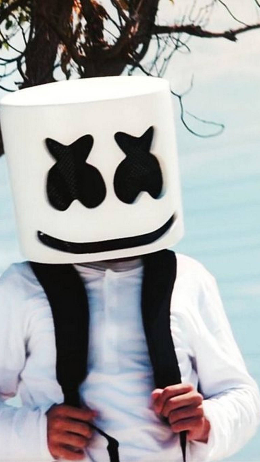 marshmello iPhone 桌布 壁紙 — 一個人戴著一個大大的白色棉花糖頭盔，有黑色眼睛和微笑，站在樹下的水邊。