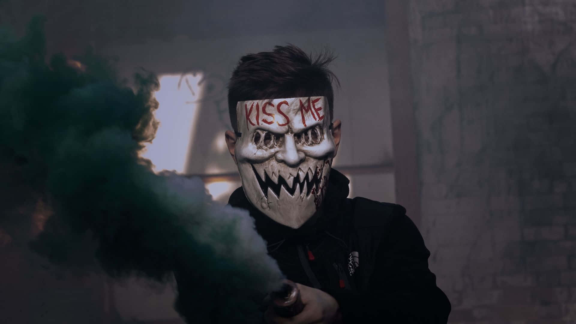 Horror Masks 桌布 壁紙 — 一個人戴著寫有「KISS ME」的骯髒面具，在昏暗的城市廢墟中手持一枚釋放綠色和白色煙霧的煙霧彈。