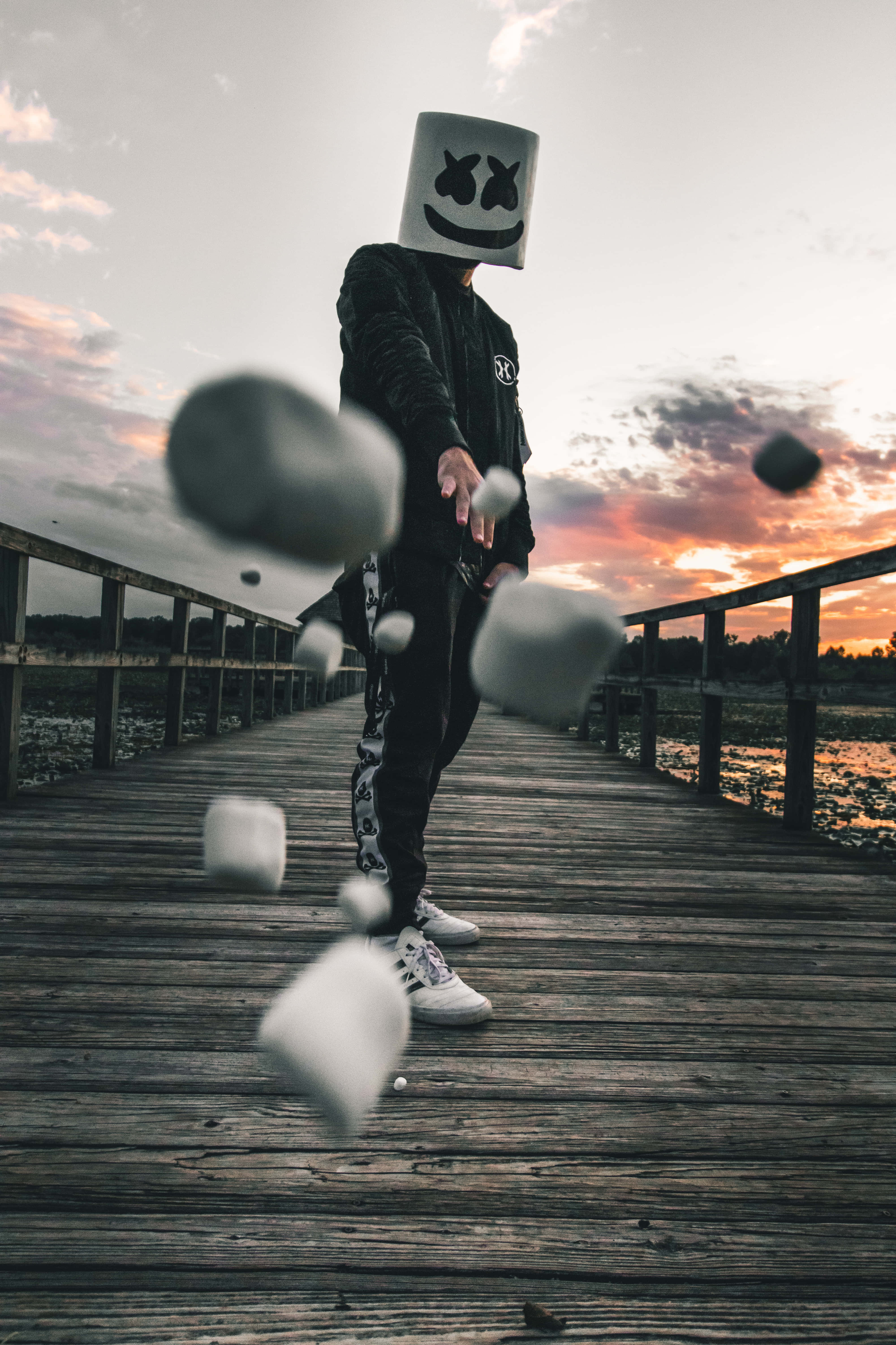 Marshmello 桌布 壁紙 — 一個人戴著棉花糖面具，在日落時分將漂浮的棉花糖扔在木製碼頭上。