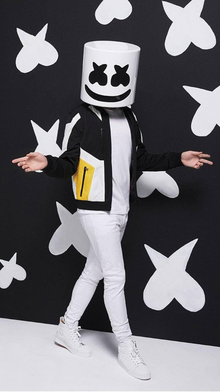 marshmello iPhone 桌布 壁紙 — 一個人戴著白色Marshmello頭盔和黑色外套，站在有白色心形圖案的黑色牆前。