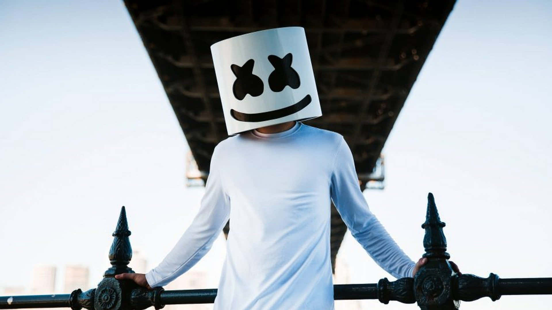 Marshmello 桌布 壁紙 — 一個人戴著白色棉花糖頭盔，站在橋欄杆下，背景是明亮的天空。