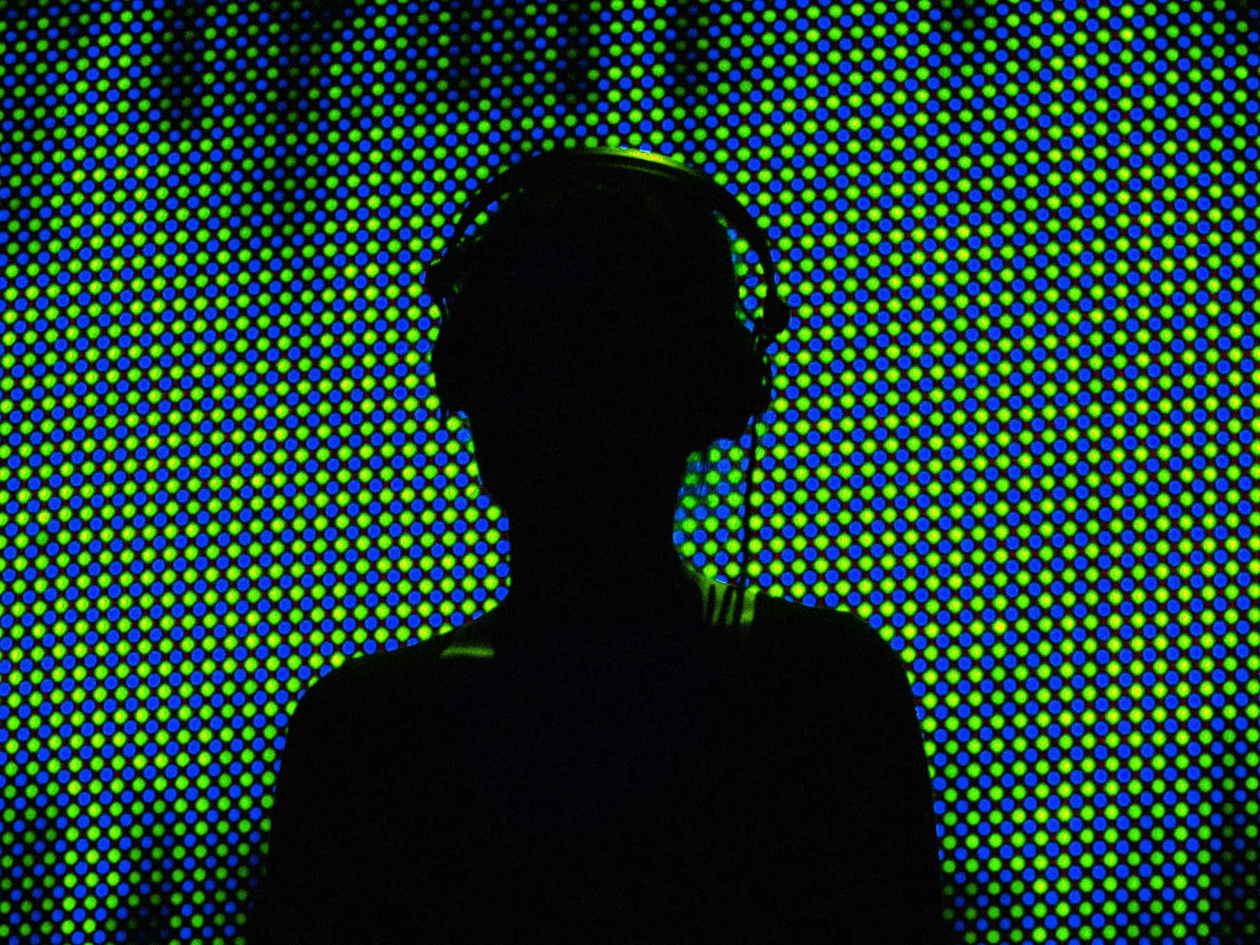DJ 桌布 壁紙 — 一個人戴著耳機的剪影，背景是充滿活力的藍色和綠色像素化LED牆。