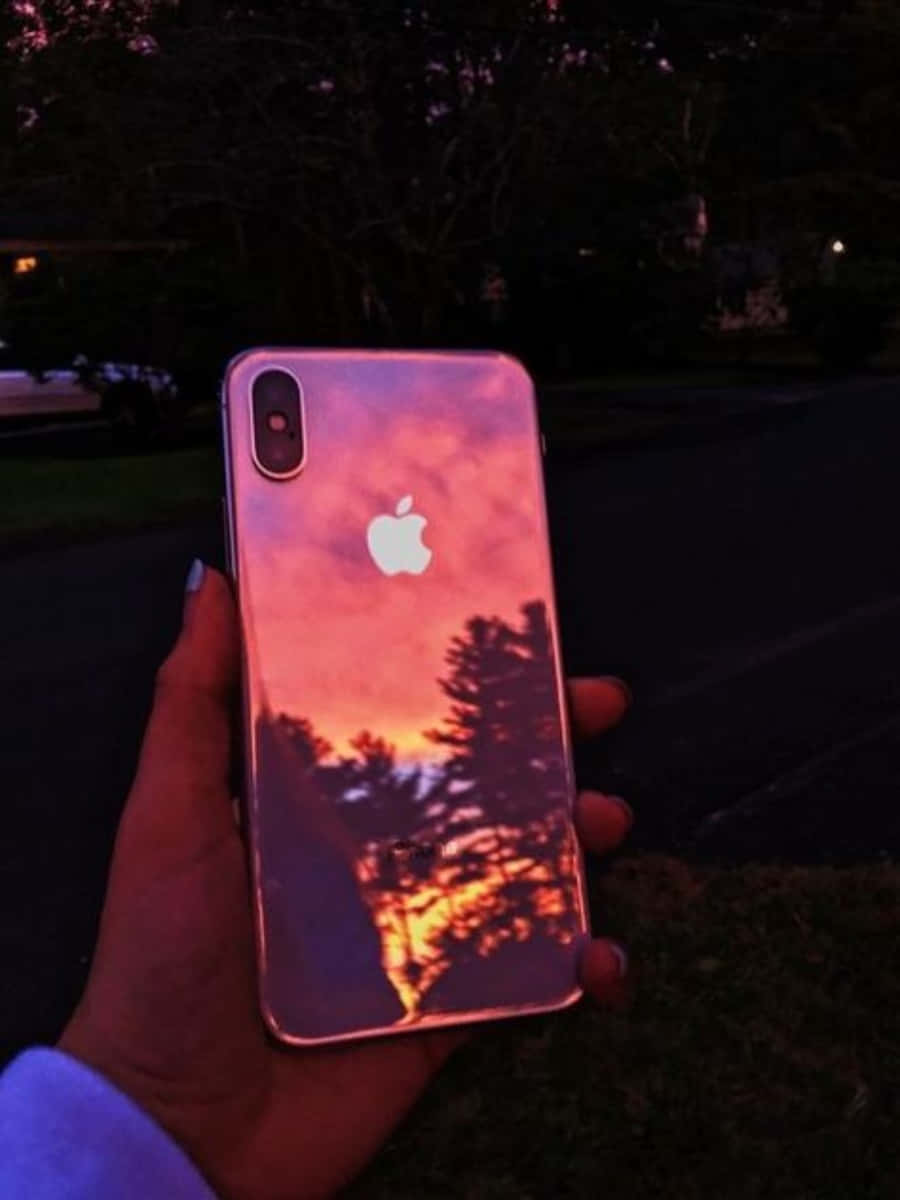 一個人手持iPhone，機身反射出日落景色 壁紙