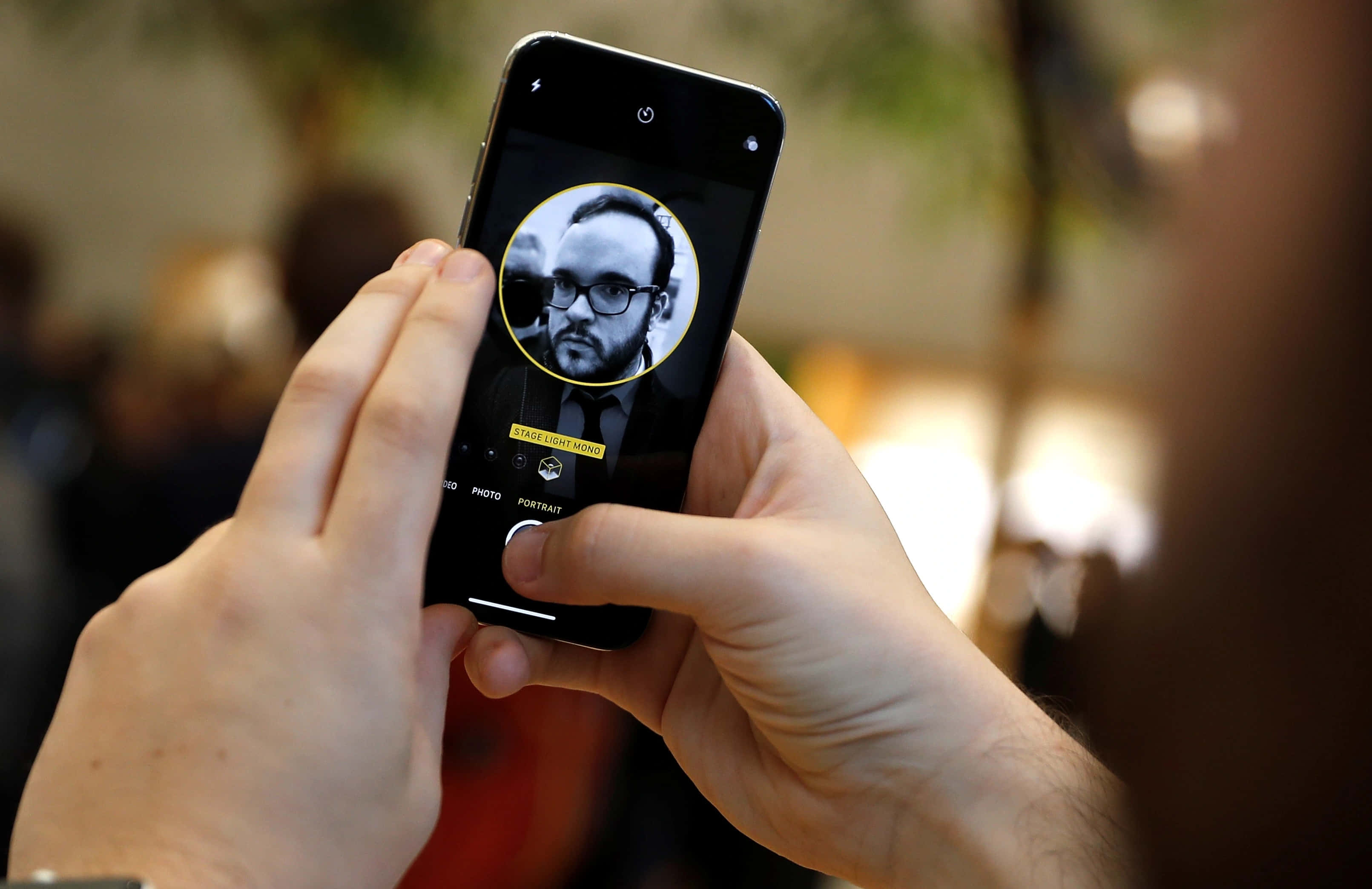 Face Id 桌布 壁紙 — 一個人手持智能手機，以人像模式顯示一位戴眼鏡和鬍鬚男士的黑白人像。