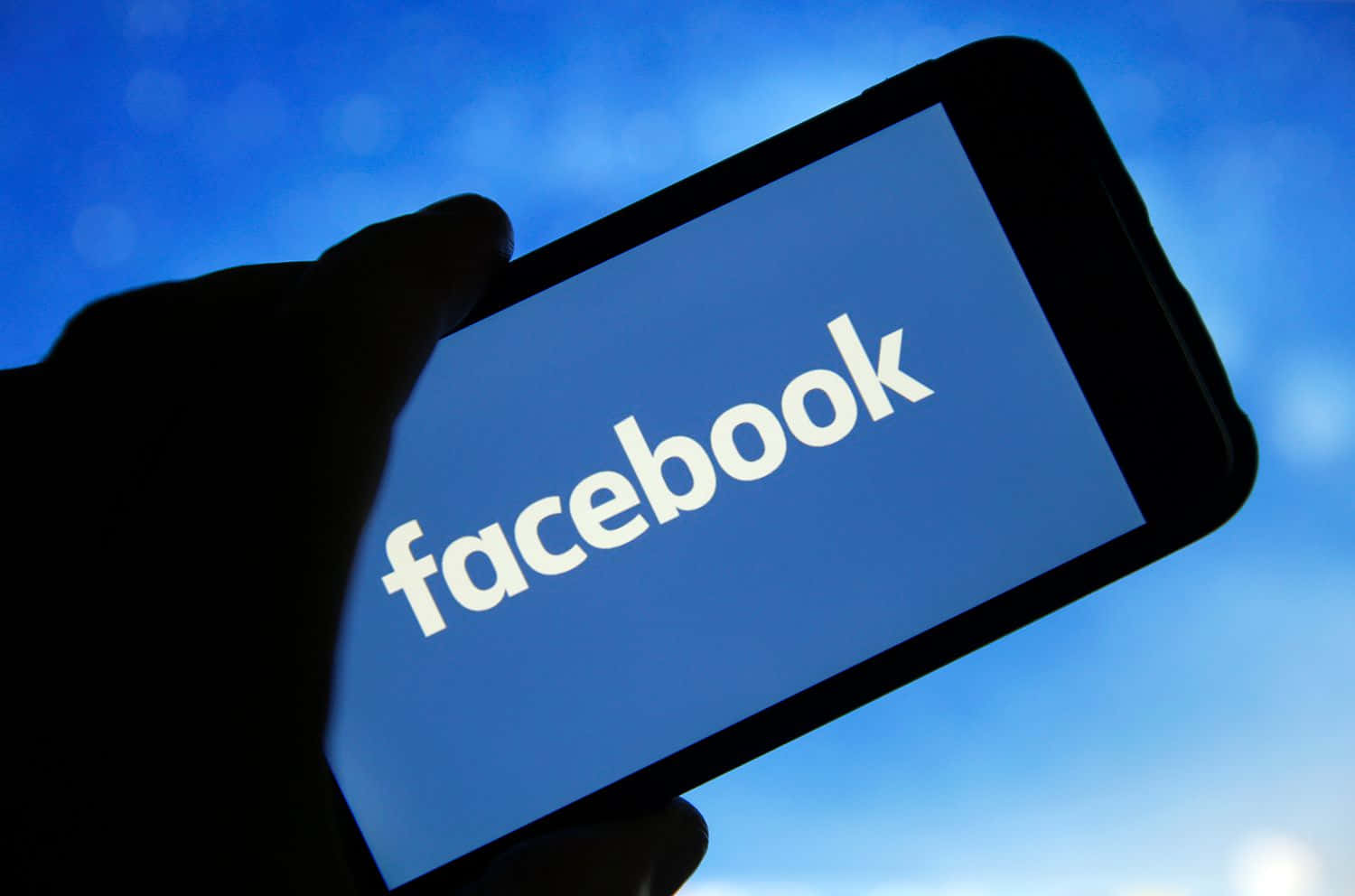 一個人手持顯示Facebook標誌的手機 壁紙