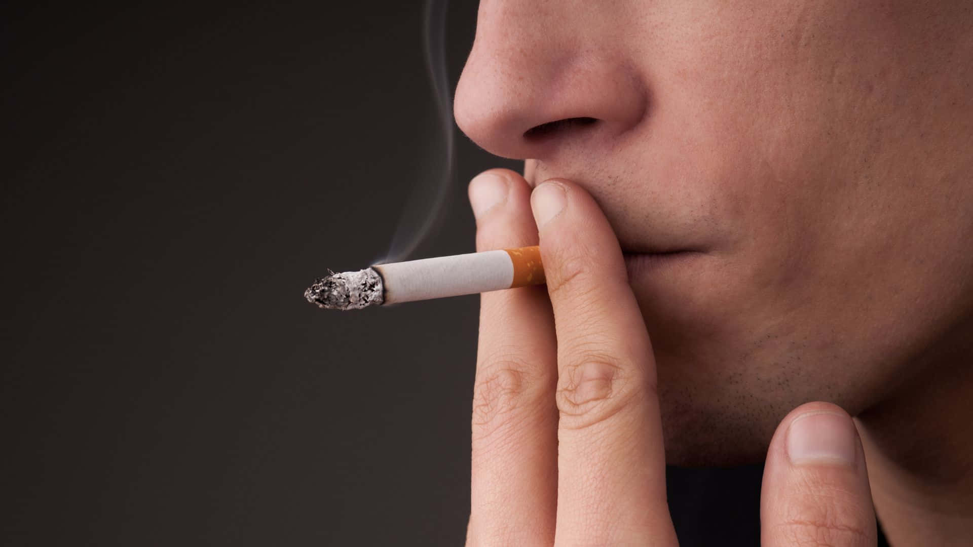 吸煙 桌布 壁紙 — 一個人手持點燃的香煙，煙霧在黑暗背景中向上繚繞的特寫。