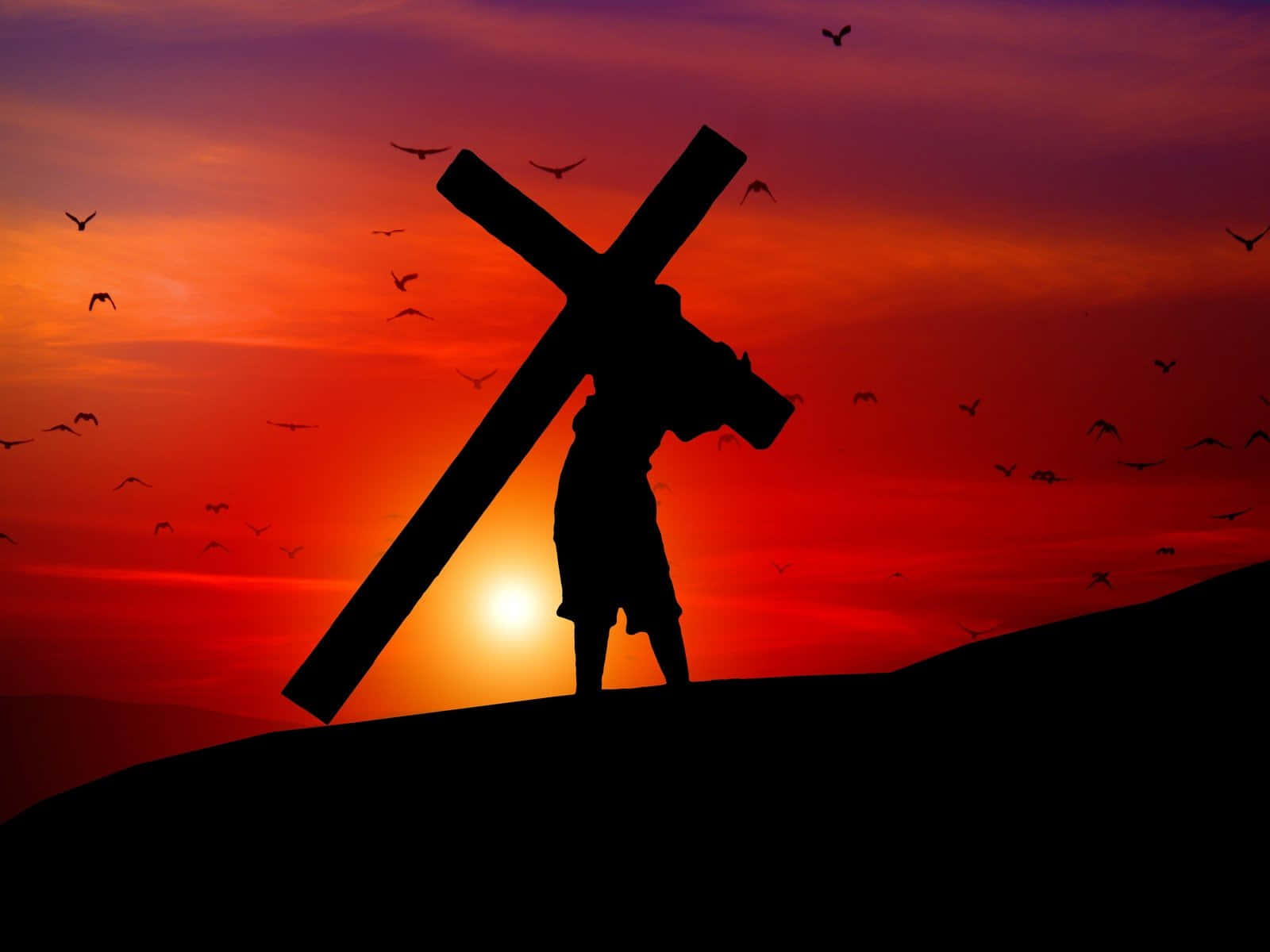 Jesus Crucifixion 桌布 壁紙 — 一個人物嘅剪影，喺山頂上扛住一個大十字架，背景係火燒般嘅日落天空，有雀仔飛緊。