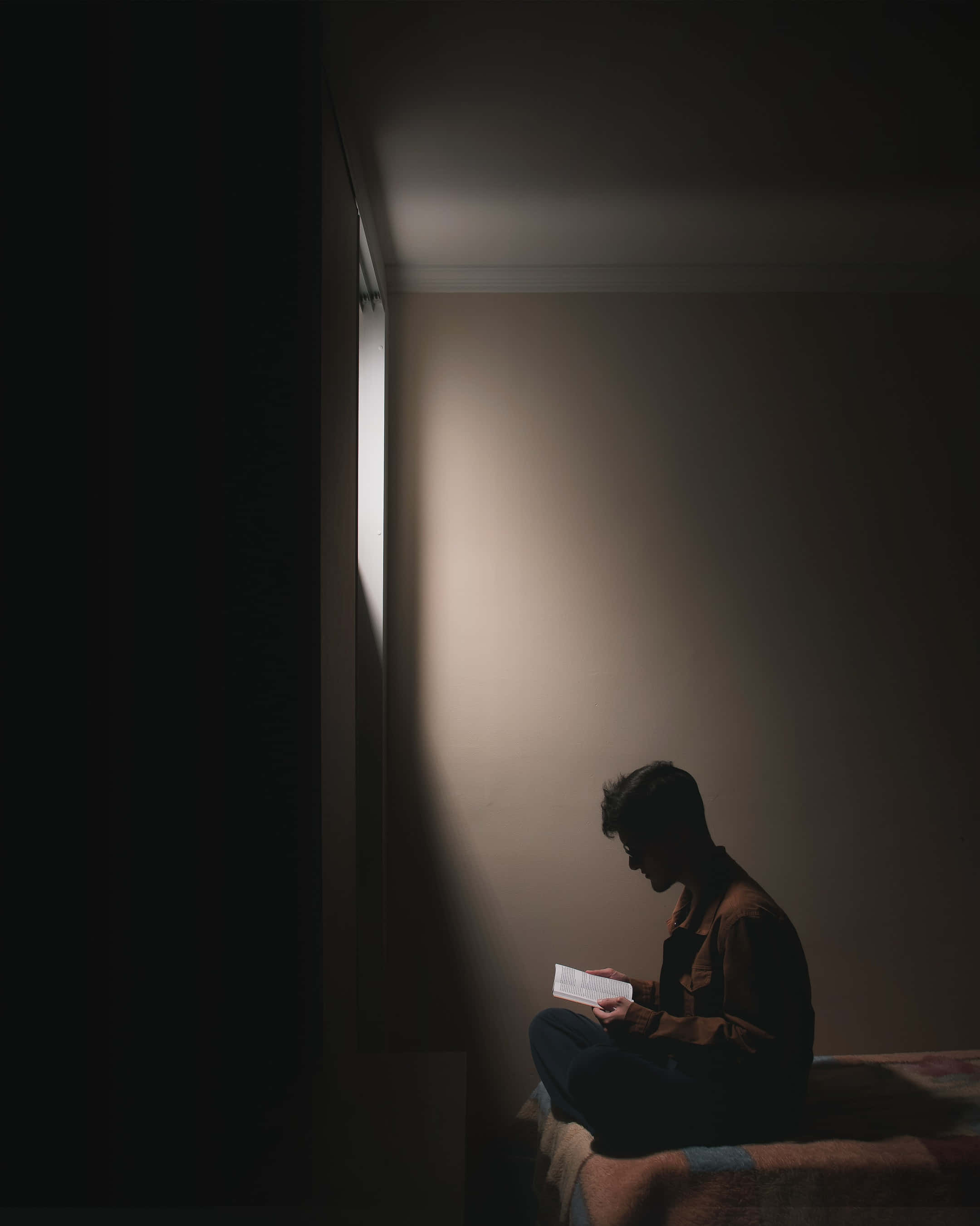 閱讀 桌布 壁紙 — 一個人獨自坐在昏暗的房間裡，被狹窄窗戶透進的柔和光線包圍，正在讀一封信。