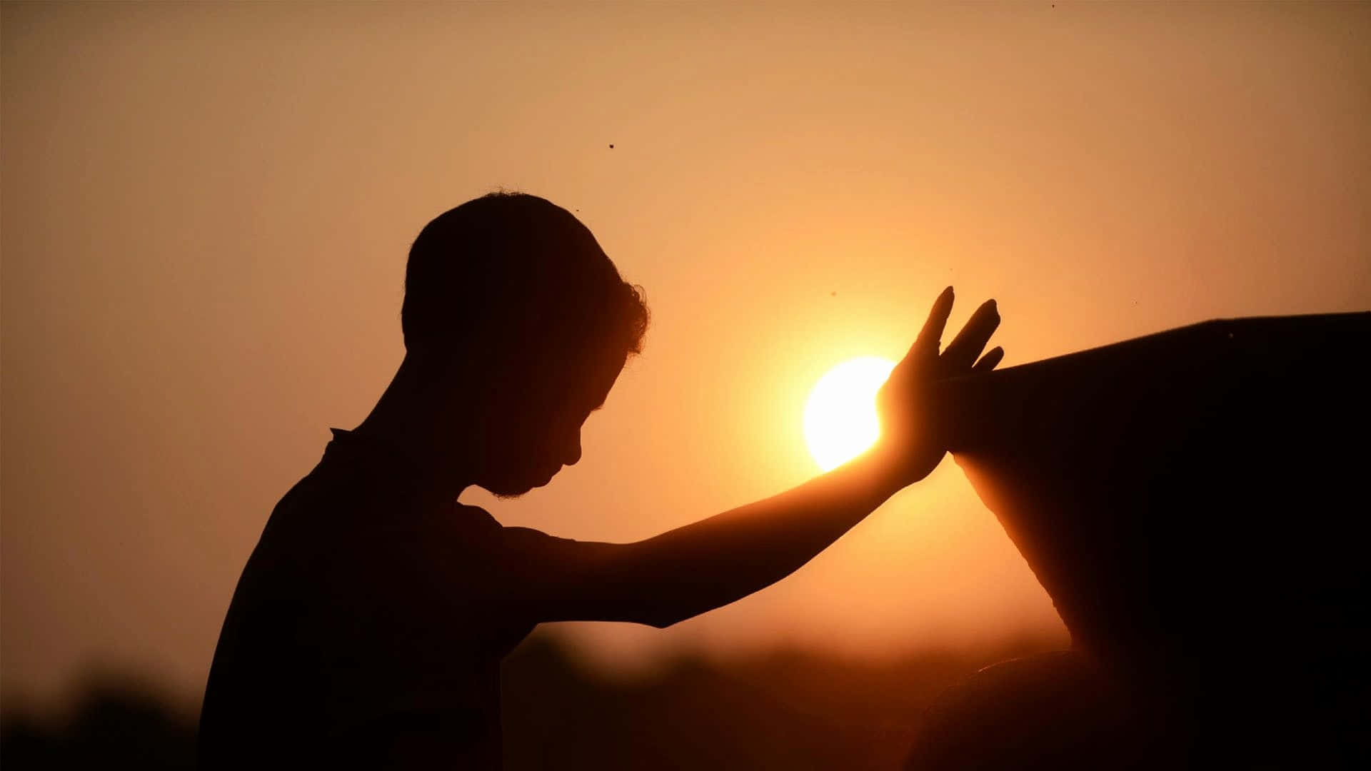 Praying 桌布 壁紙 — 一個人的剪影，在日落時分伸出手臂朝向太陽，手掌張開，映襯著溫暖的橙色天空。
