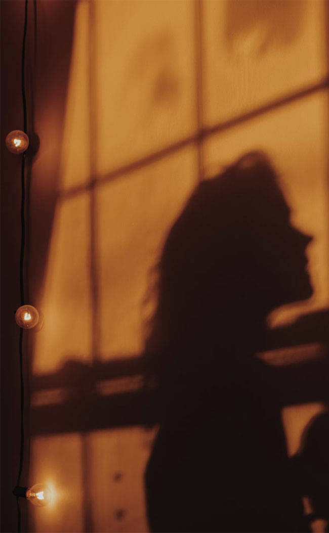 Silhouette 桌布 壁紙 — 一個人的剪影凝視著窗外，窗戶沐浴在串燈溫暖的金色光芒中，投射出柔和的陰影。