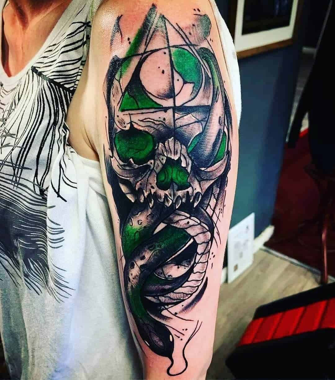 Death Eaters 桌布 壁紙 — 一個人的手臂上展示了一個詳細的骷髏頭紋身，帶有綠色眼睛和一條盤繞的蛇，以黑色、灰色和鮮綠色墨水繪製。