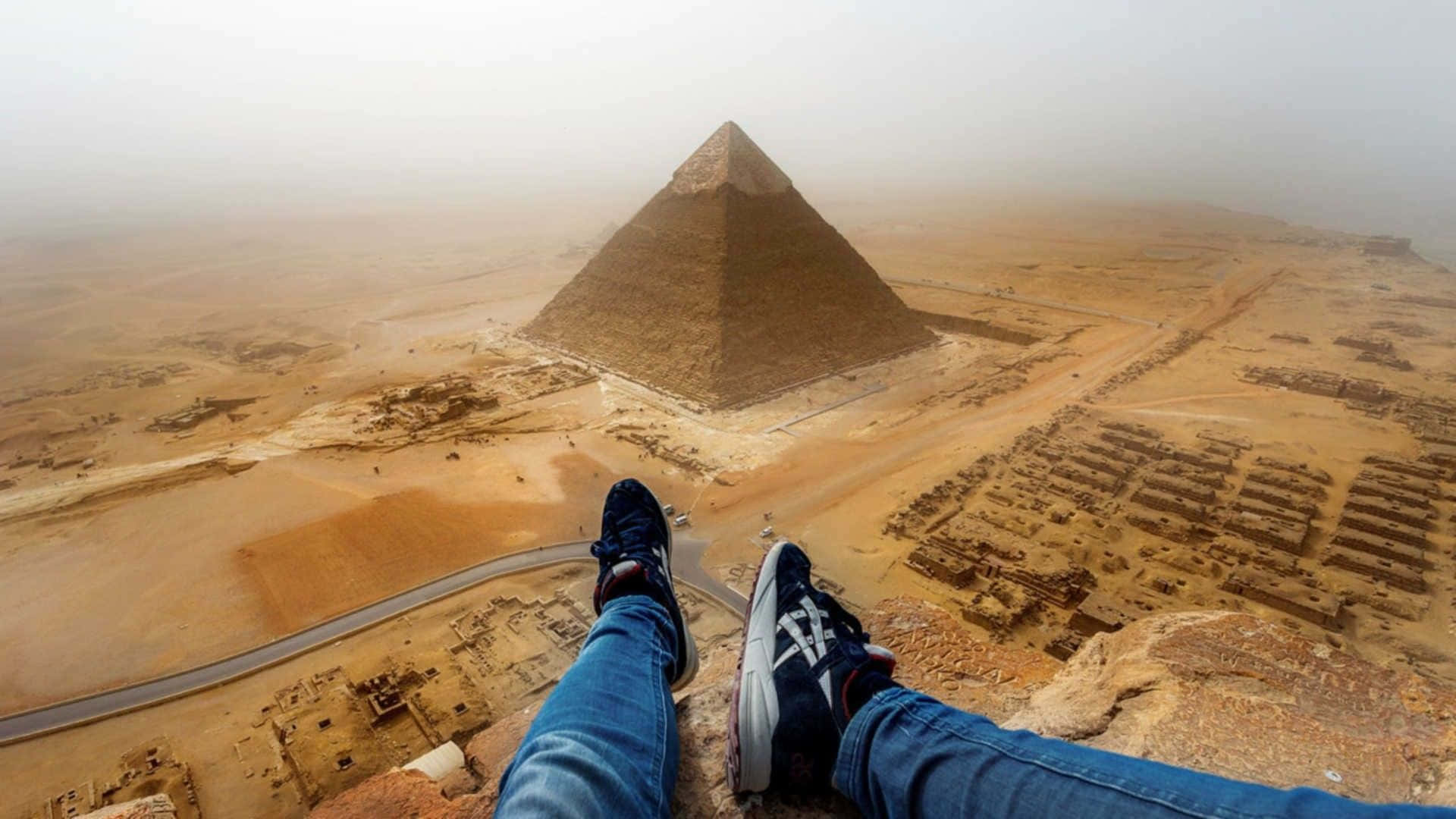 Egypt 桌布 壁紙 — 一個人的腳穿著運動鞋，擱在懸崖上，俯瞰著籠罩在沙漠薄霧中的吉薩大金字塔。