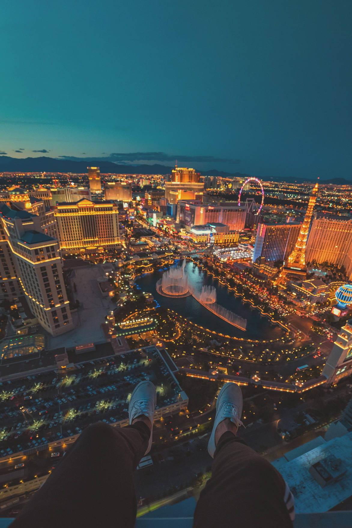 Las Vegas Night 桌布 壁紙 — 一個人的雙腳懸掛在屋頂上，俯瞰著暮色中燈火輝煌的拉斯維加斯大道。