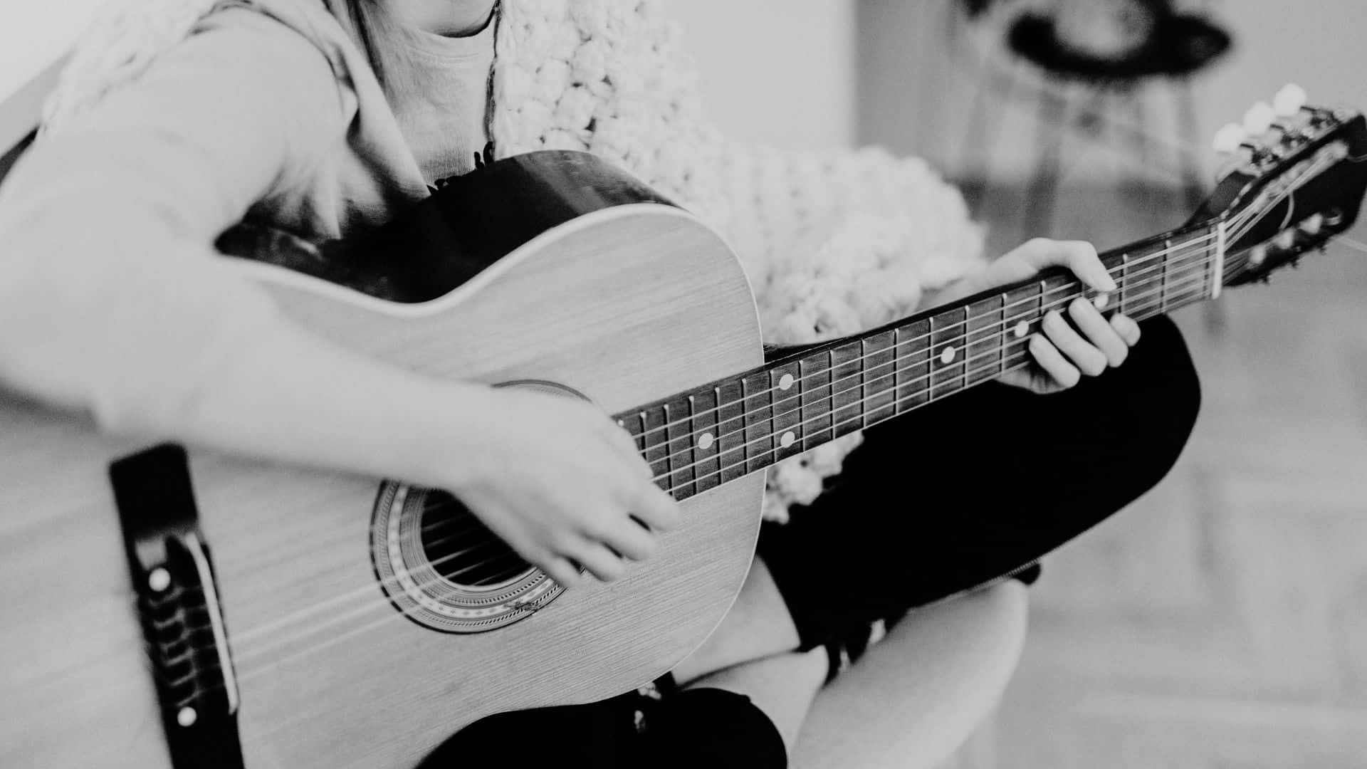 Black And White Guitar 桌布 壁紙 — 一個人盤腿坐著，在舒適的單色室內環境中彈奏木結他。