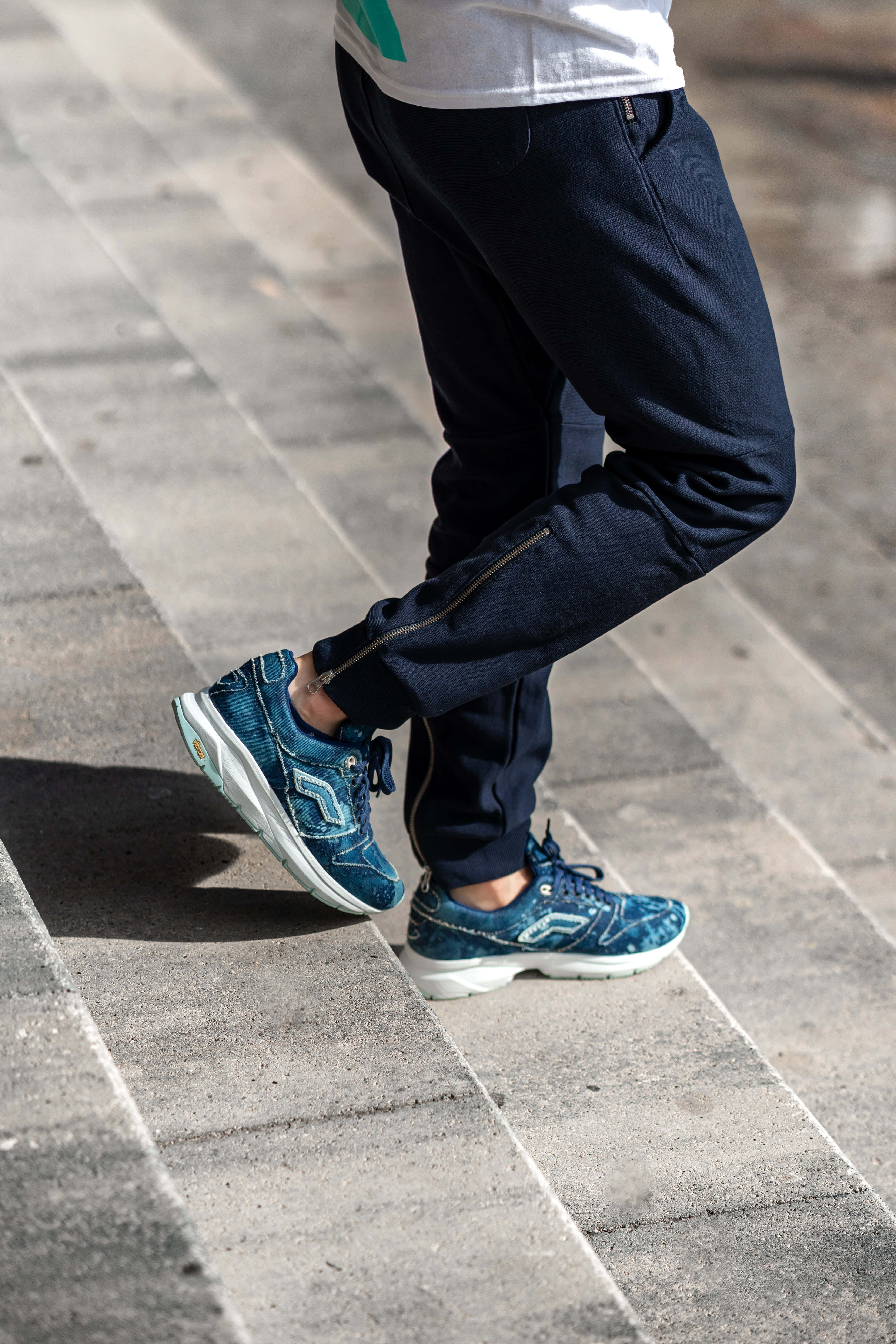 Navy Blue Shoes 桌布 壁紙 — 一個人穿著海軍藍慢跑褲和藍色運動鞋嘅雙腳踩喺灰色石鋪路面上嘅特寫。