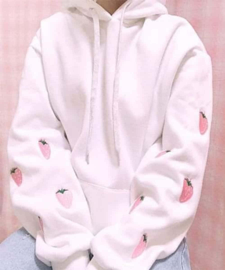 Pink Sweater 桌布 壁紙 — 一個人穿著白色連帽衫，袖子上有粉紅色草莓刺繡，背景是柔和的粉紅色。