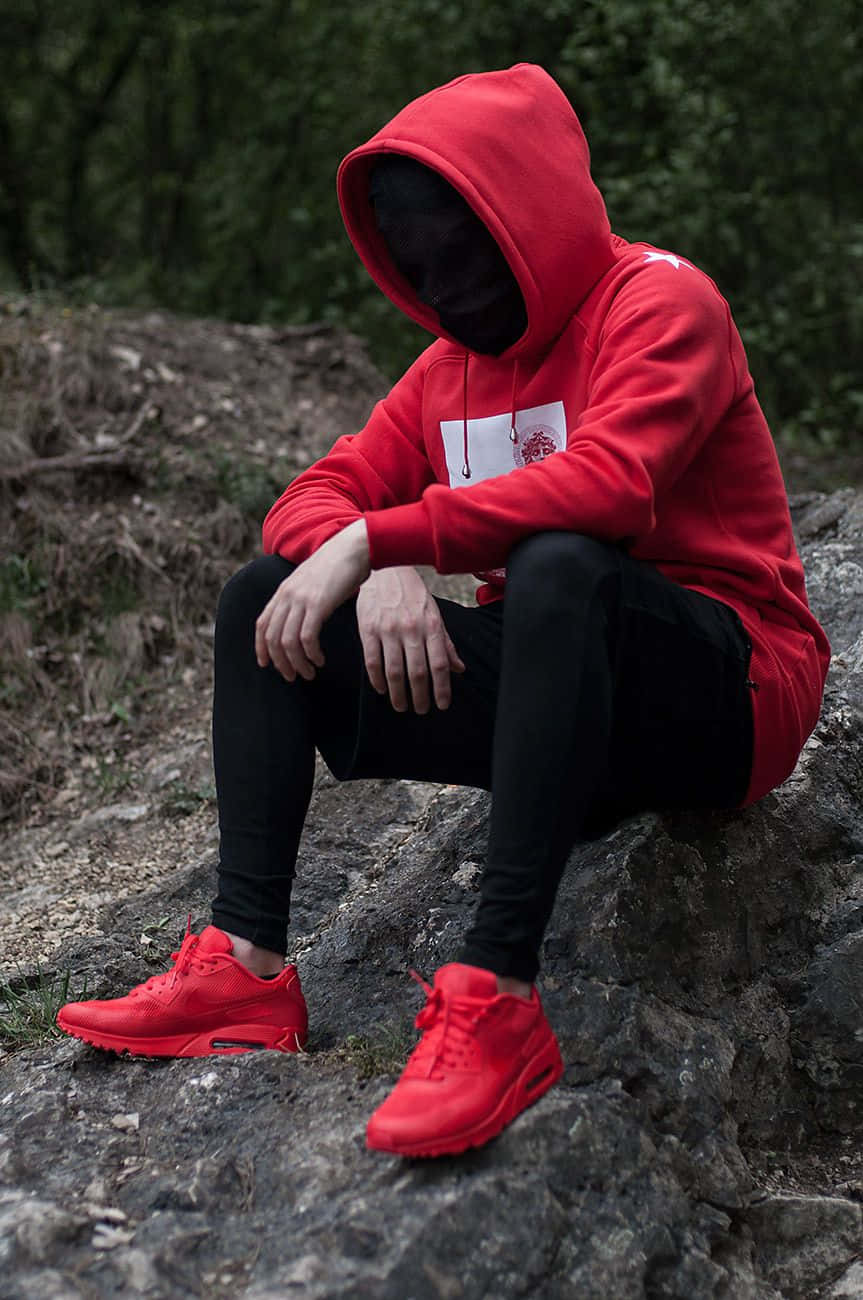 Red Hoodie 桌布 壁紙 — 一個人穿著紅色連帽衫和相配的運動鞋，獨自坐在岩石山坡上，臉部被陰影遮蓋。