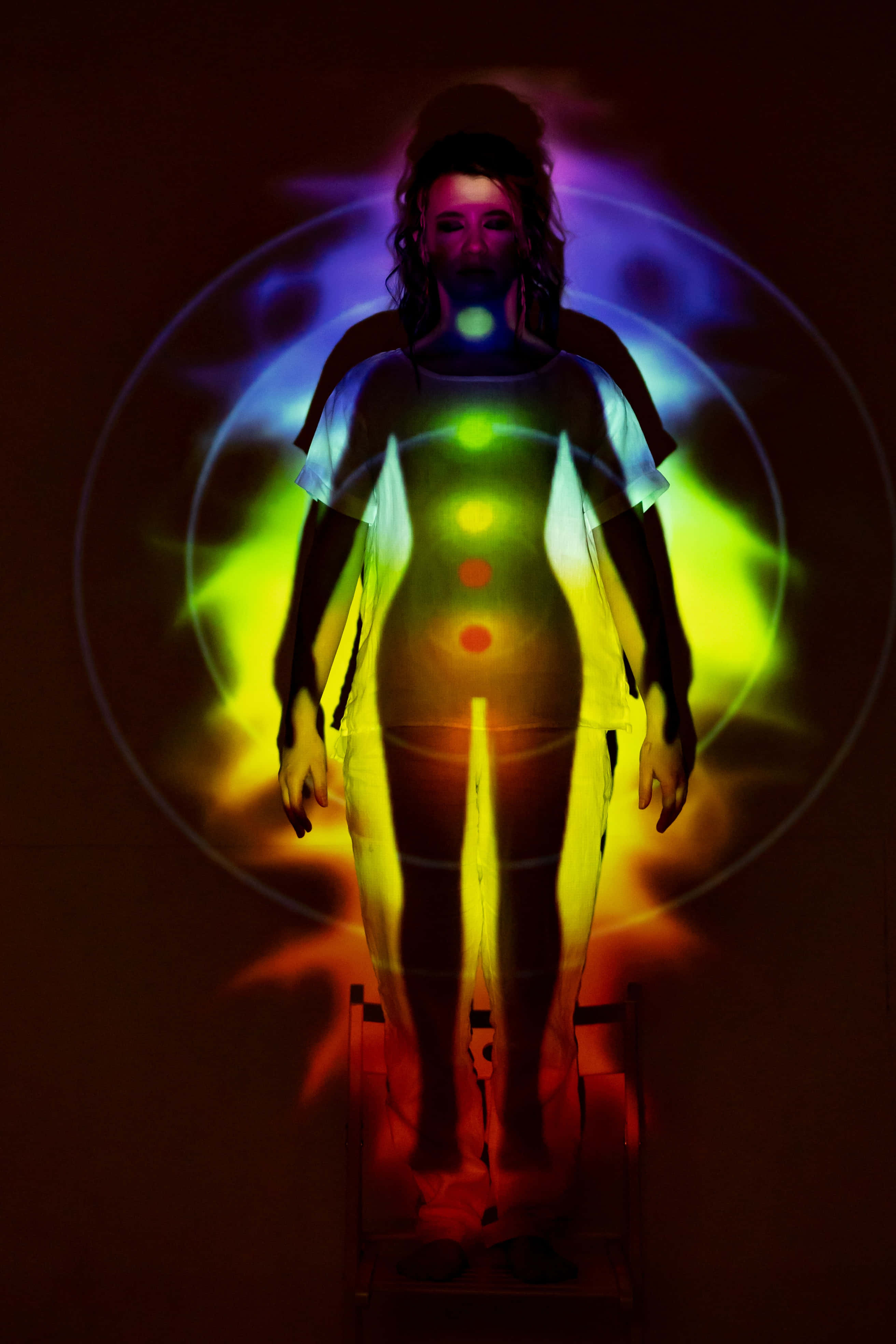 Reiki 桌布 壁紙 — 一個人站在黑暗背景前，被發光的脈輪和輻射能量圈照亮。