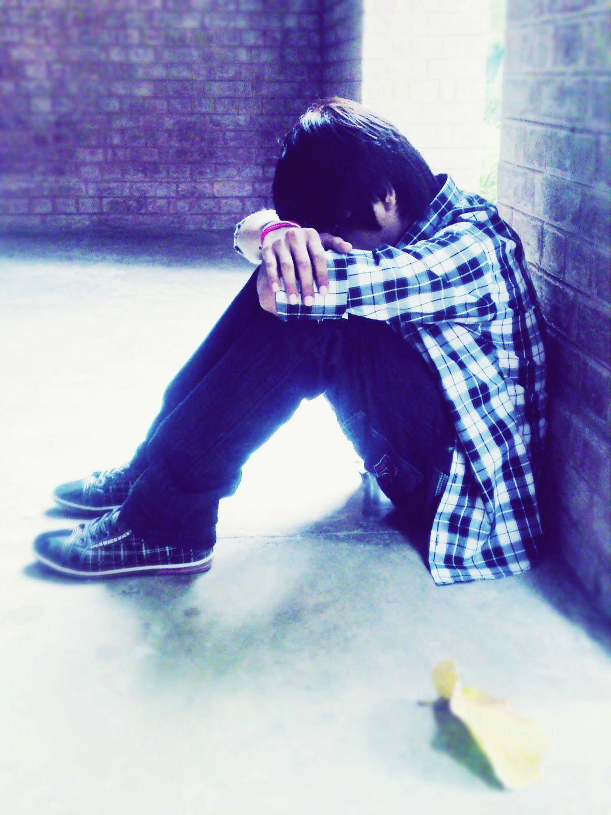 emo 桌布 壁紙 — 一個人蜷縮在昏暗小巷的磚牆上，低著頭，穿著格仔襯衫和深色褲子。