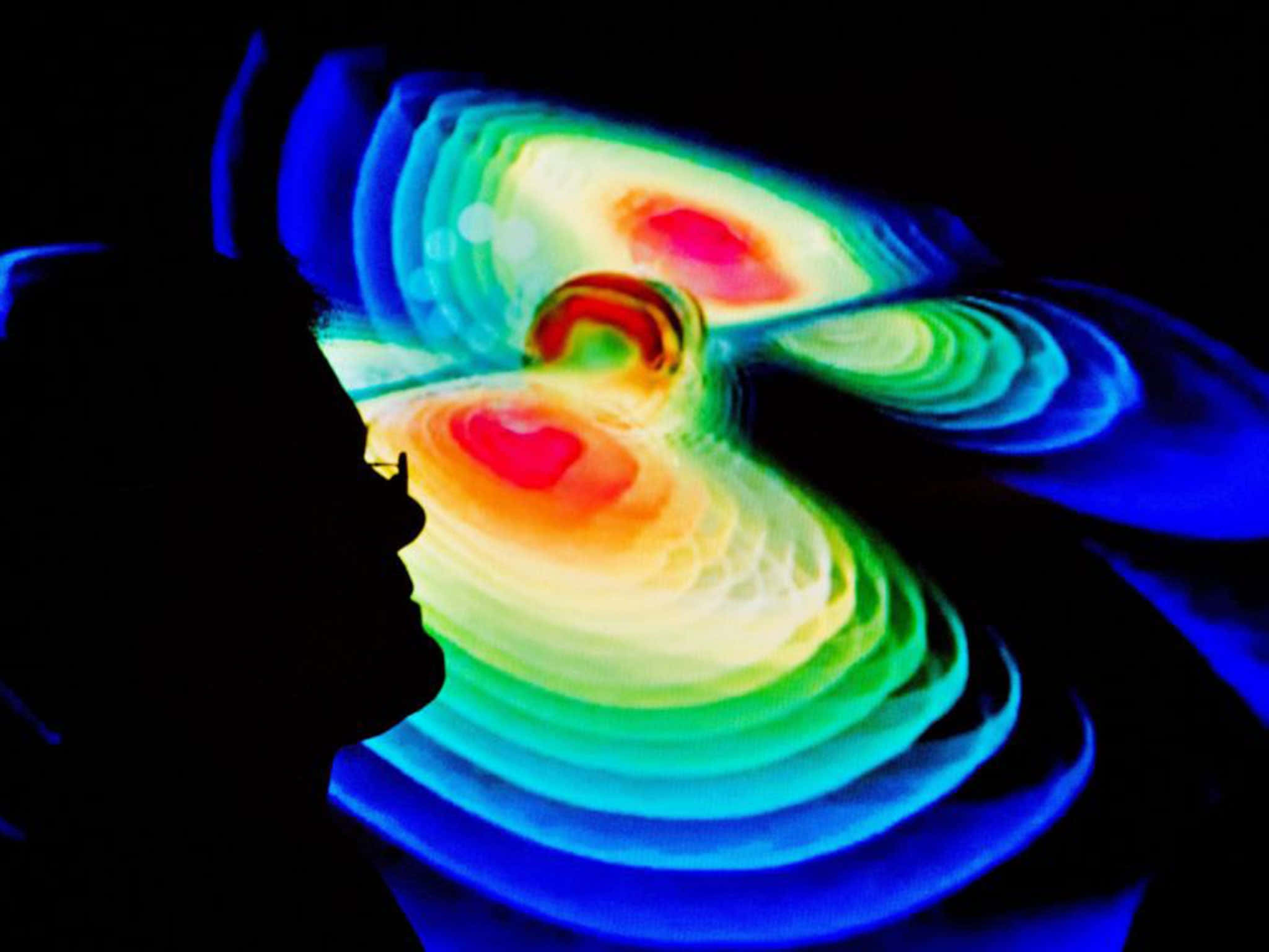 Gravitational Waves 桌布 壁紙 — 一個人觀察著充滿活力、旋轉的抽象燈光展示的剪影，背景為黑色，帶有同心彩虹波紋。