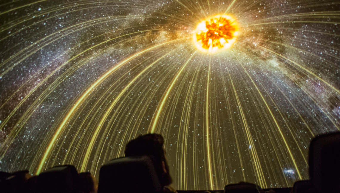 Planetarium 桌布 壁紙 — 一個人觀看在弧形圓頂天花板上帶有金色條紋和發光星星的耀眼星爆投影。