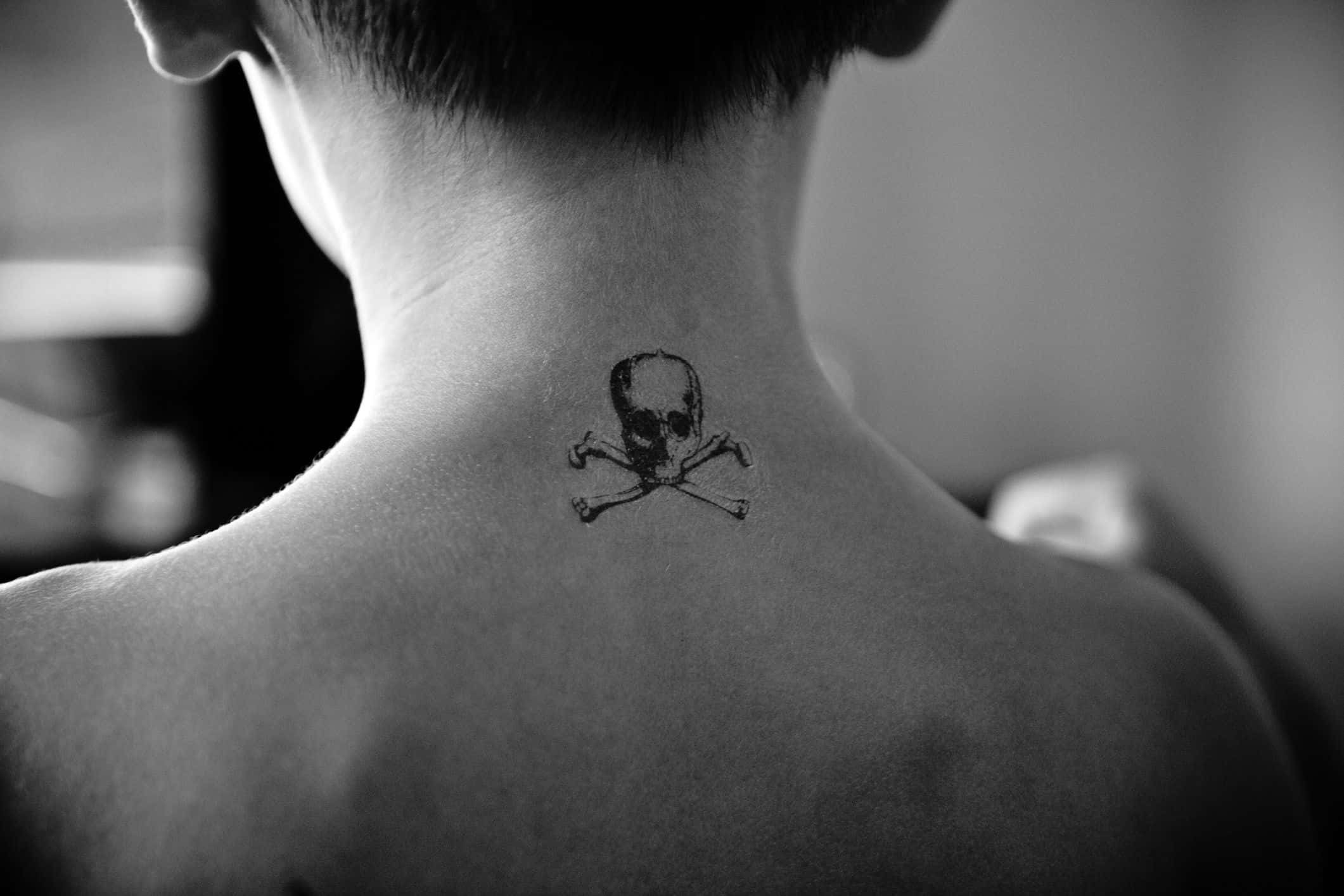 Halloween Tattoos 桌布 壁紙 — 一個人頸部嘅黑白特寫，上面有個細細嘅骷髏頭同交叉骨紋身。