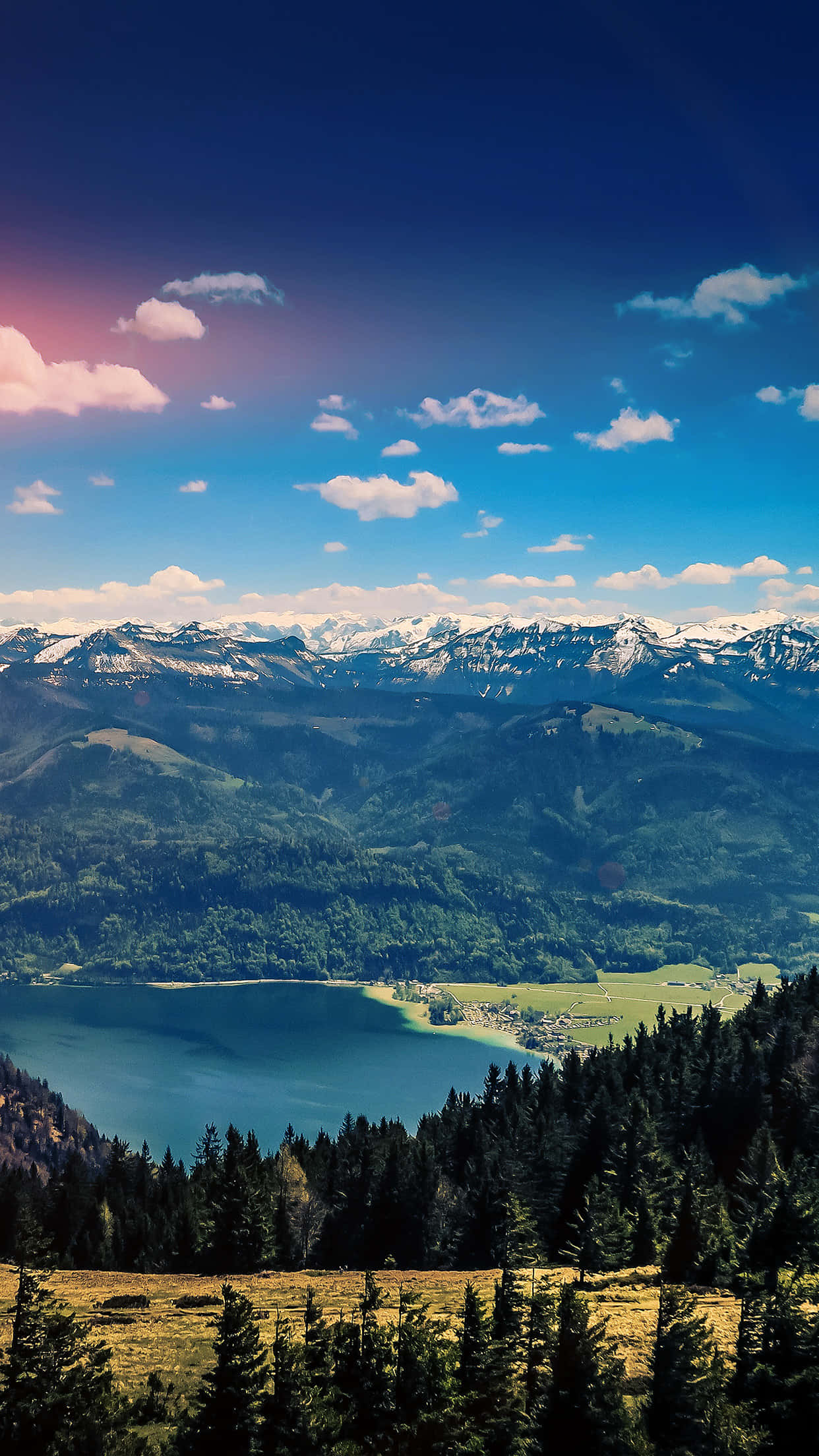 Nature Scenery 桌布 壁紙 — 一個令人嘆為觀止的山谷，有一個藍綠色的湖泊，坐落在白雪覆蓋的山峰和茂密的森林之間，在湛藍的天空下，點綴著幾朵雲彩。