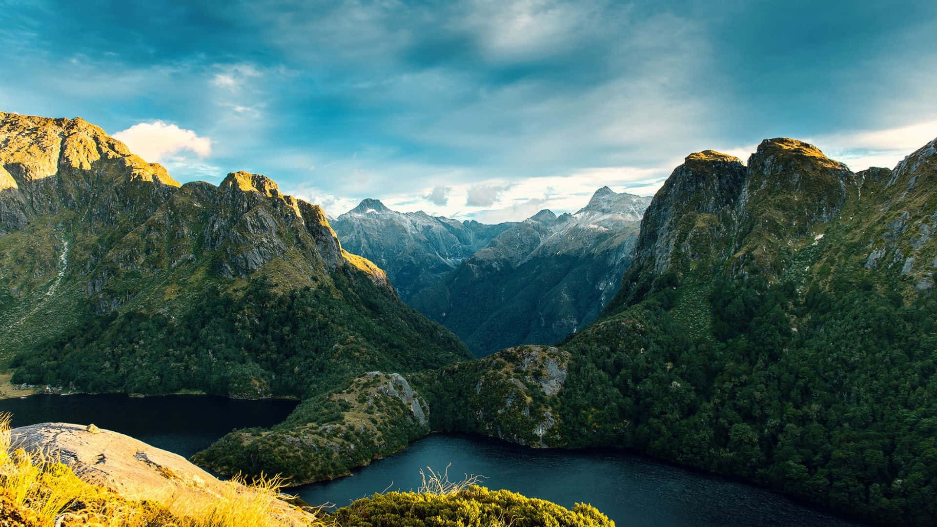Beautiful Mountain 桌布 壁紙 — 一個令人嘆為觀止的山谷，深藍色的湖泊坐落在崎嶇的綠色山峰之間，天空壯麗。