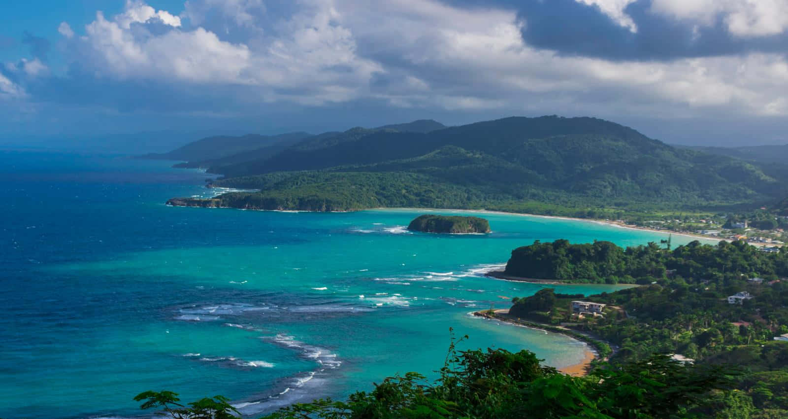 Jamaican Island 桌布 壁紙 — 一個令人嘆為觀止的海岸海灣，碧綠的海水 nestled 在鬱鬱蔥蔥的綠色山丘之間，天空烏雲密布，氣勢磅礴。